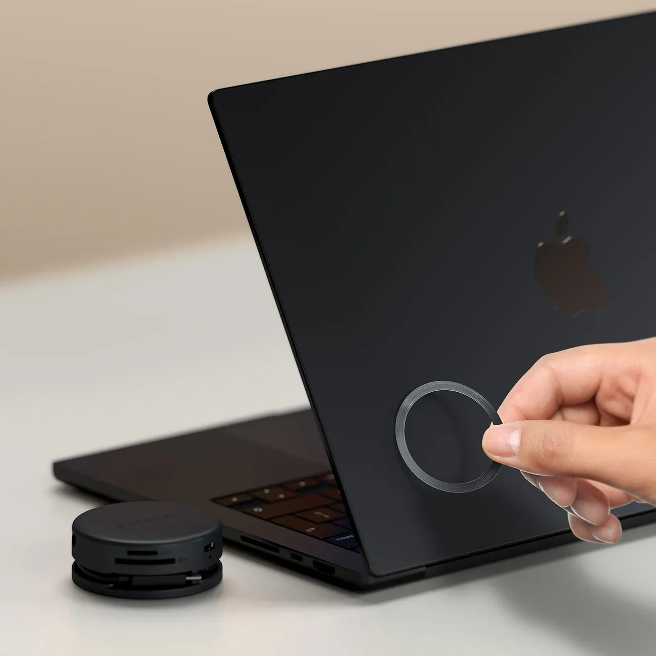 A hand attaching 3M Adhesive Ring directly to MacBook Pro for the Satechi OntheGo™ 7-in-1 Multiport Adapter to connect to.