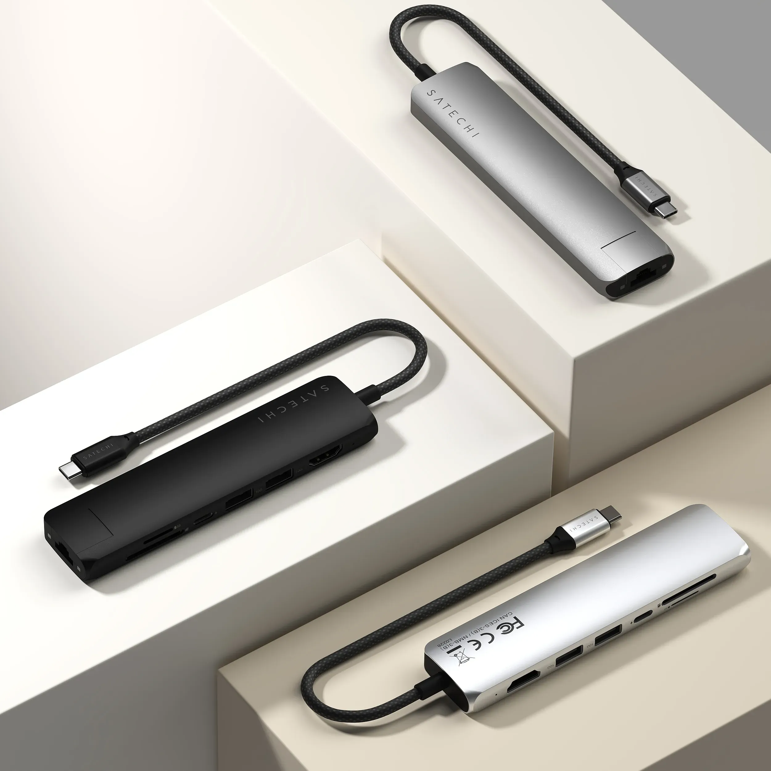Three Satechi 7-in-1 USB-C Slim Multiport Adapter with Ethernet in Silver, Space Gray, and Black on three different platforms.