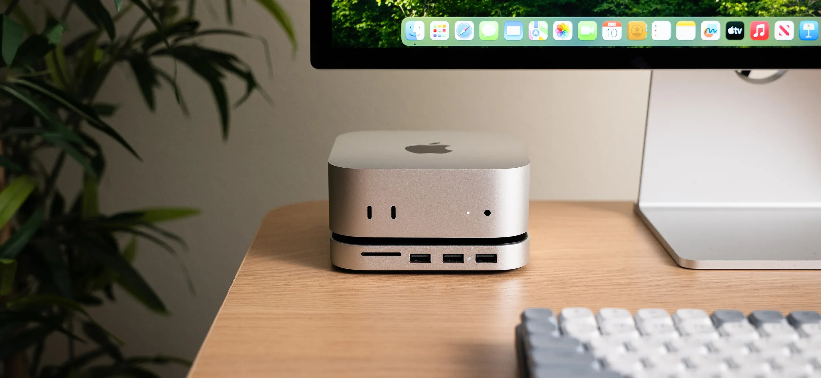 A Satechi Mac Mini M4 Stand and Hub with SSD Enclosure next to a iMac, keyboard, and house plant.