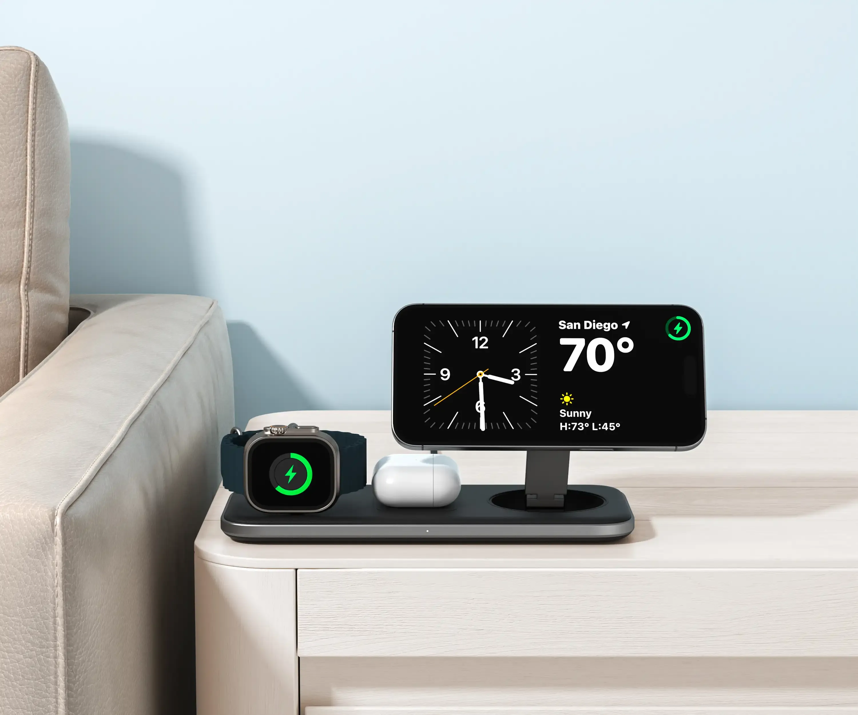 Qi2 Trio Wireless Charging Pad on a wooden side table beside a couch, wirelessly charging an iPhone, AirPods, and an Apple Watch simultaneously.