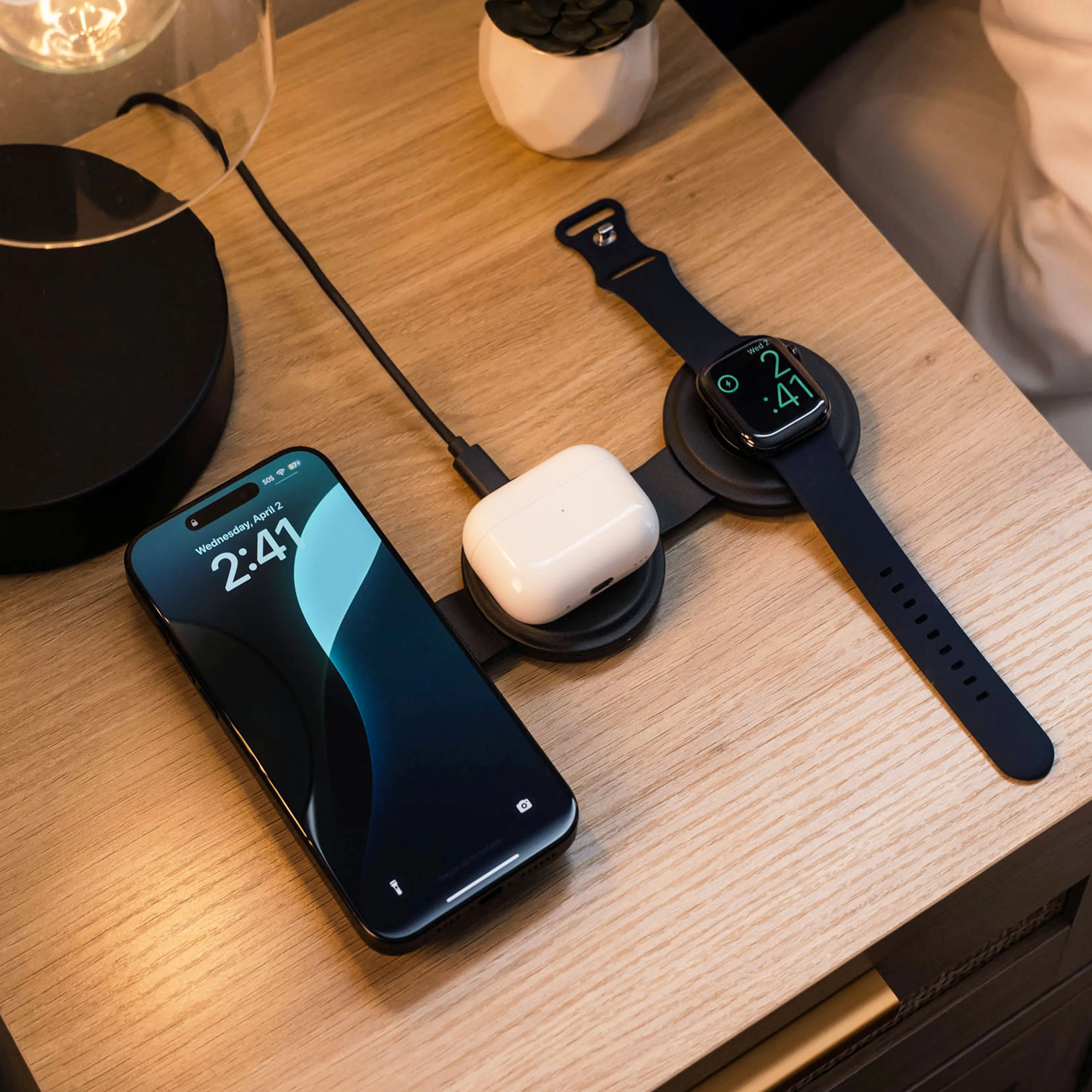 A Satechi OntheGo™ 3-in-1 Charger charging an iPhone, AirPods, and Apple Watch on bedside table.