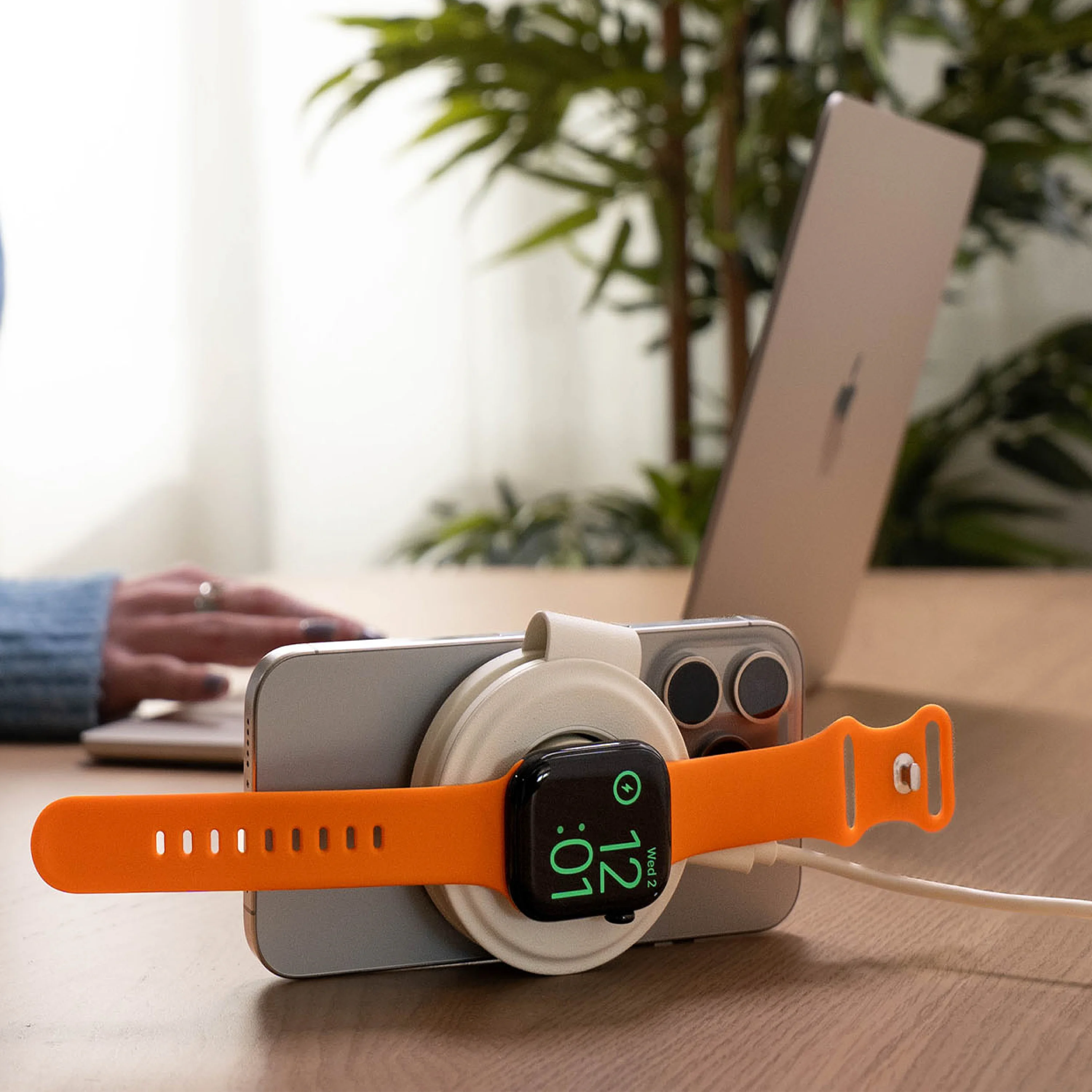A OntheGo™ 2-in-1 Charger in Sand, simultaneously charging an Apple Watch with an orange band and an iPhone.