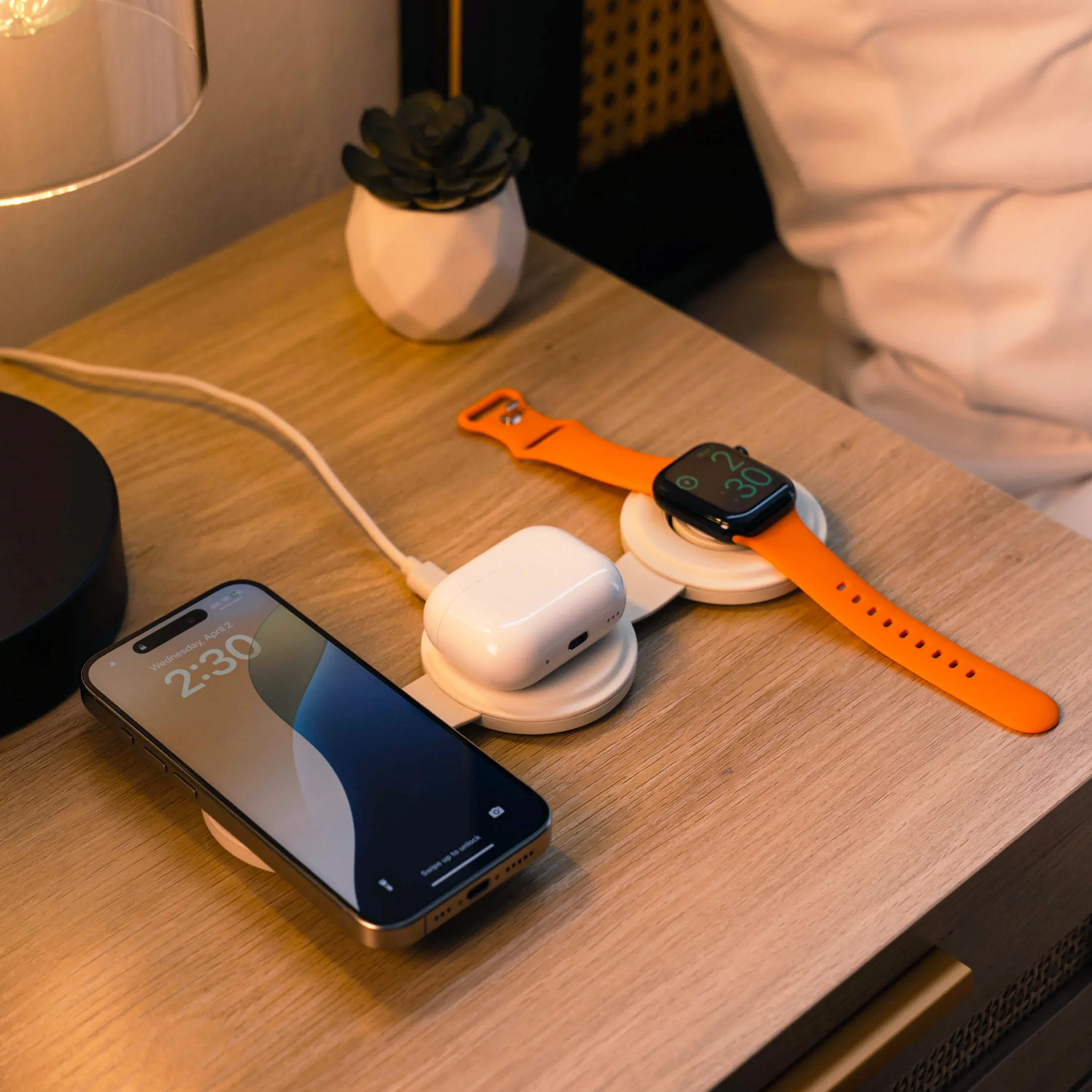 A Satechi OntheGo™ 3-in-1 Charger laying flat on a bedside table, charging an iPhone, AirPods, and Apple Watch simultaneously.