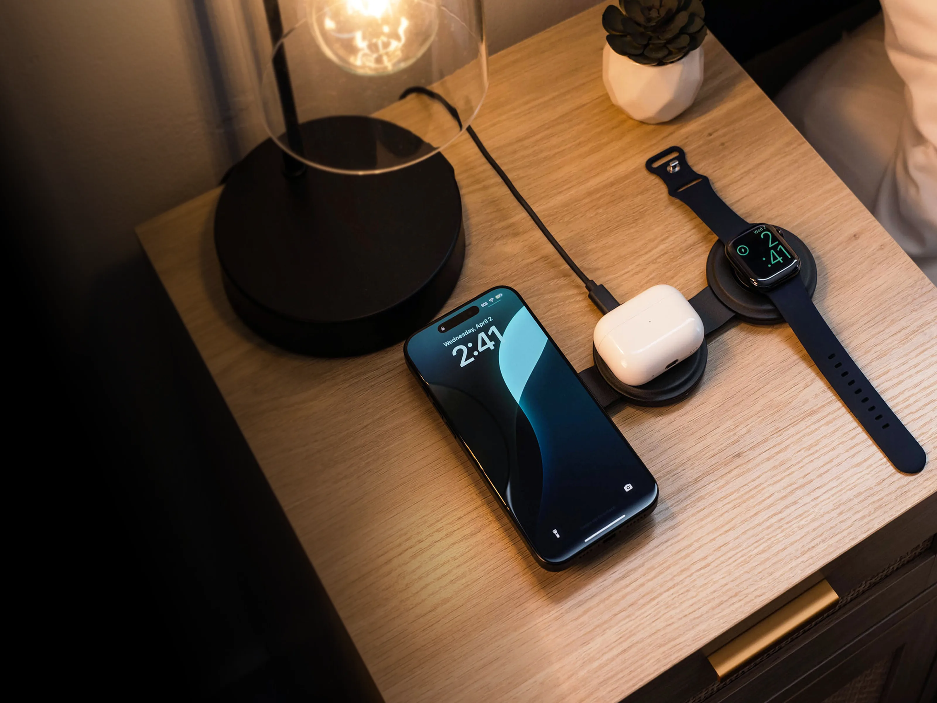 A Satechi OntheGo™ 3-in-1 Charger  charging a iPhone, AirPods, and Apple Watch on a nightstand.