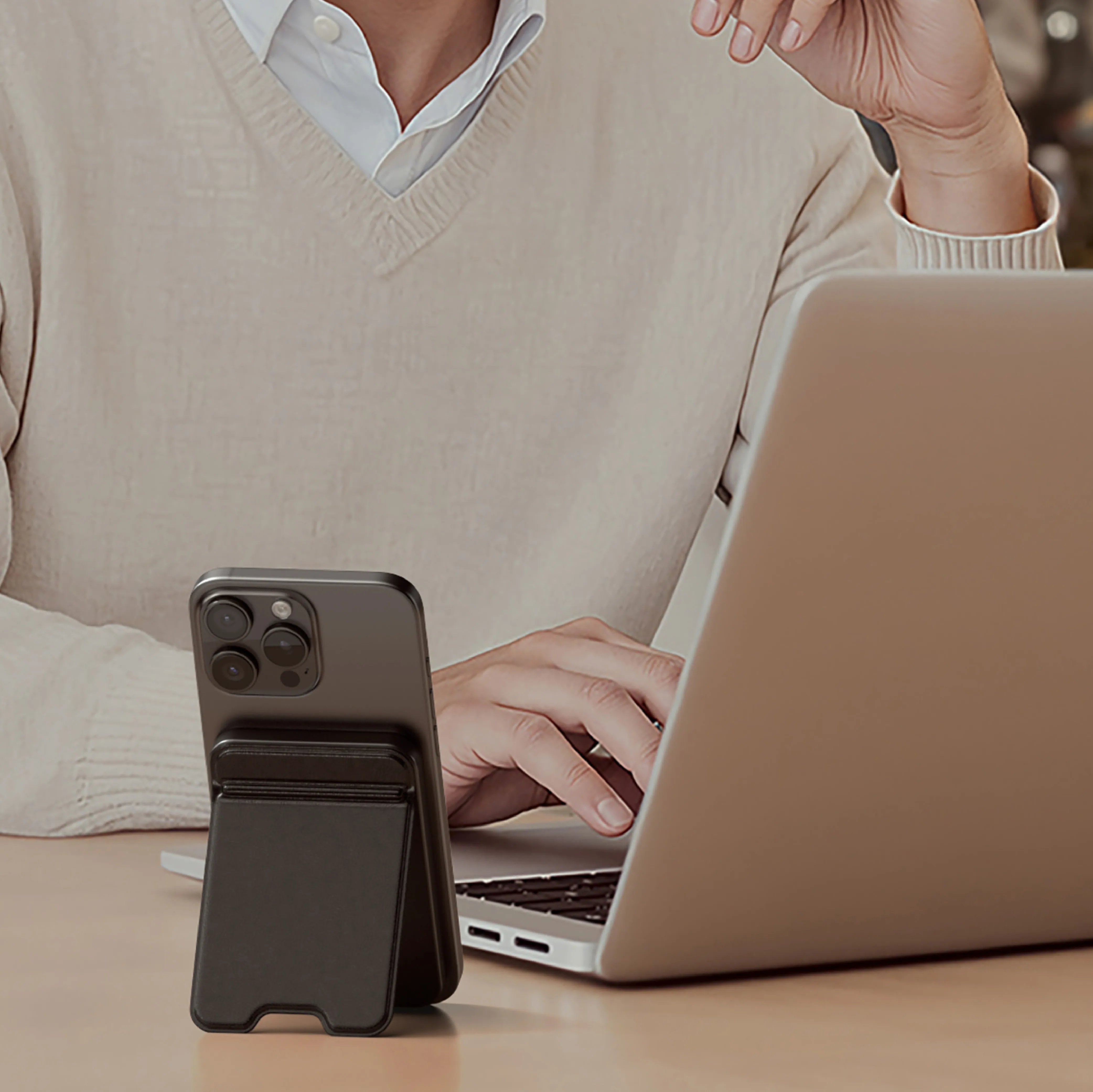 A person typing on a MacBook while their iPhone is propped upright on a Satechi On-the-Go™ Power Bank with Stand.