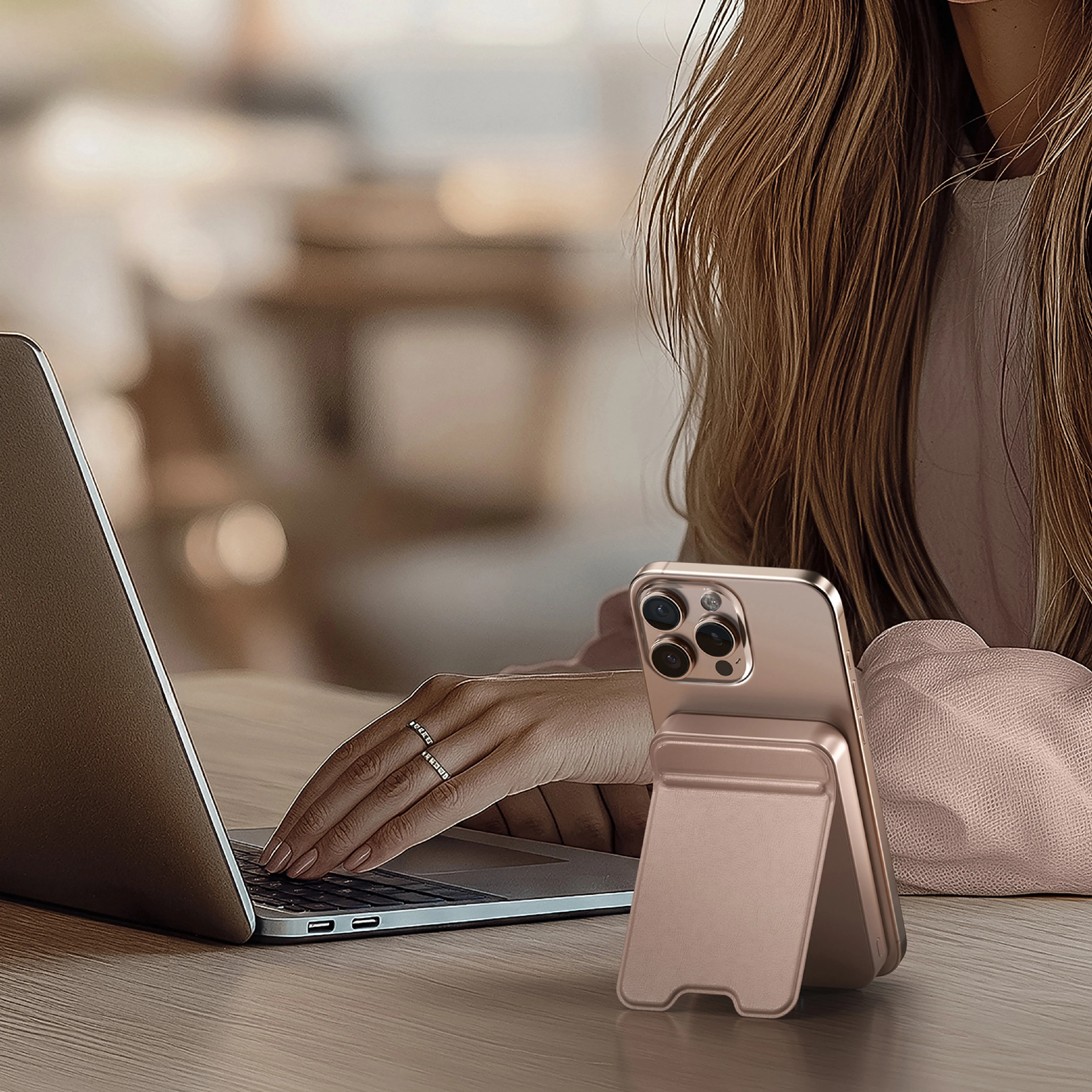 A person typing on a MacBook with a Satechi OntheGo™ Power Bank (10K) in Desert Rose placed nearby, charging an attached iPhone.