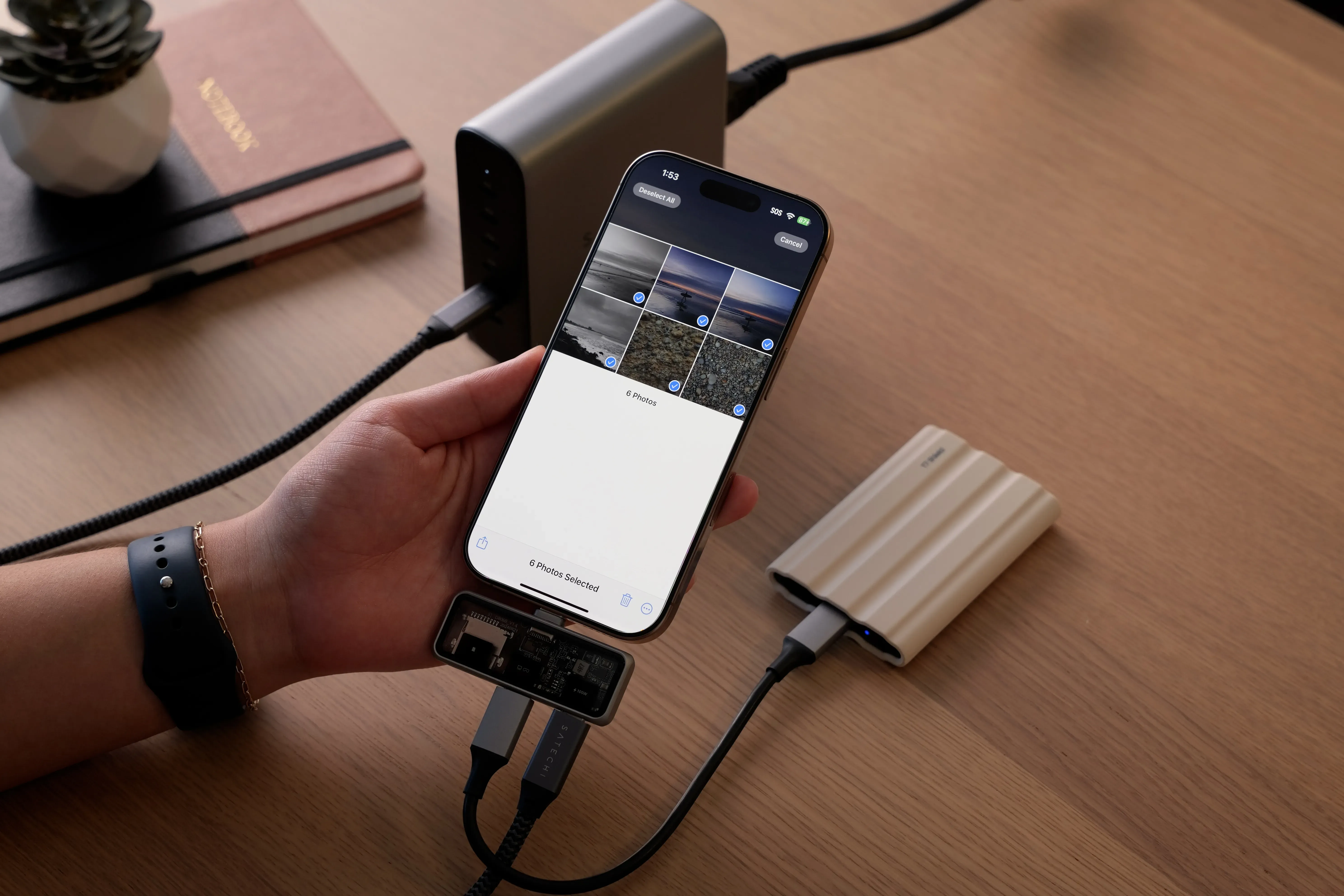 Hand holding a Satechi Mobile XR Hub with microSD, connected to an iPhone 16 Pro Max and transferring photos to an external hard drive.