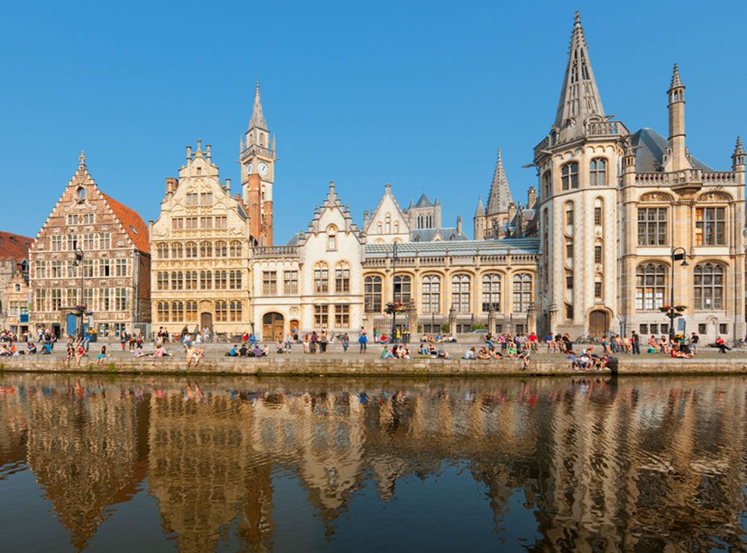 In Belgium, ornate guild houses face a busy walking trail along a river.