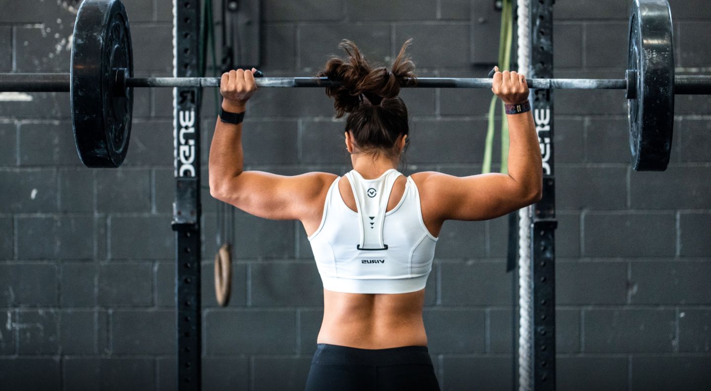 The back of a strong woman as she lifts a heavy weight over her head