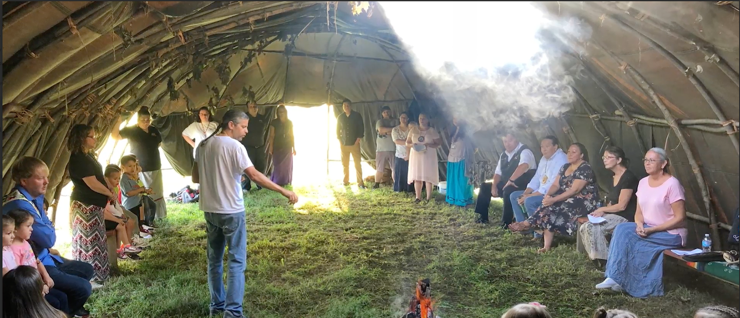 A group of people attending a Native American ritual under a tent where a fire is lit