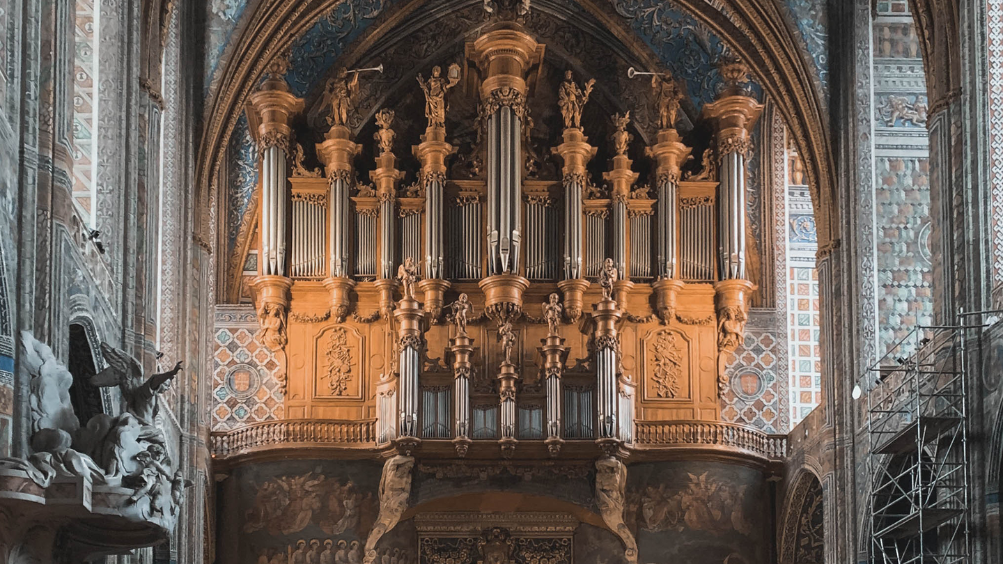 Antique pipe organ with engravings, and angel statues inside Notre Dame church in Paris