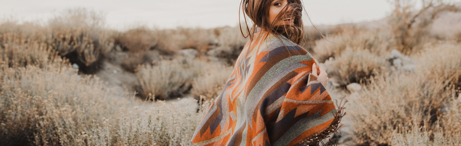 A woman walking through a filed wearing a colorful poncho