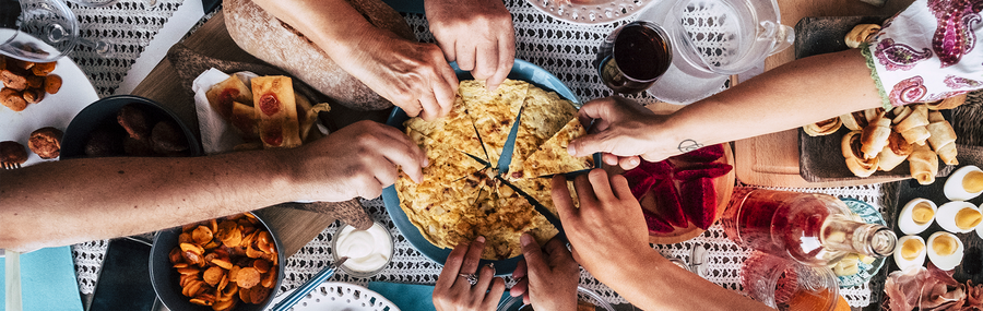 A decorated dinner table with lots of dishes and people taking bread from a communal plate