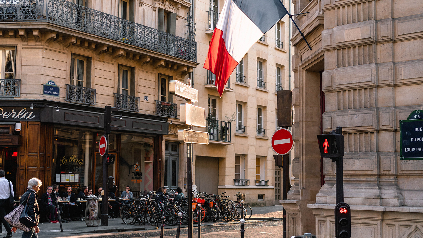 A street corner in French with a café and a French flag flying form an entry way
