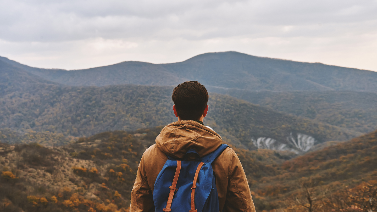 A young man wearing a blue backpack hiking through hills