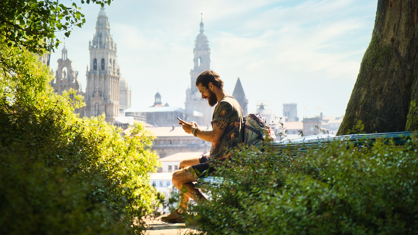 A young man looking at his phone with tall cathedral towers in the background