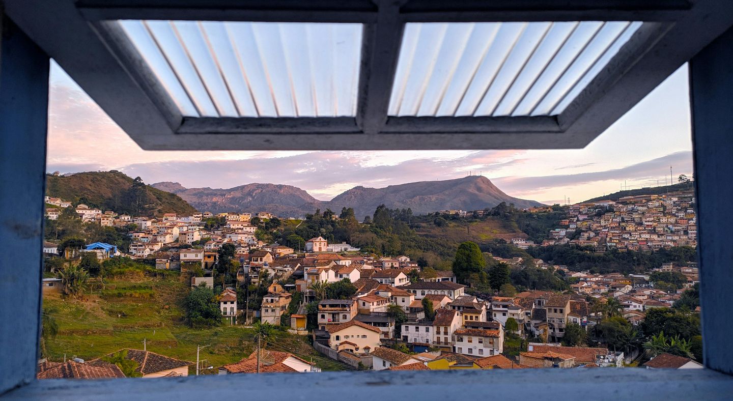 the view through an open window reveals a picturesque, tile-roofed town in the mountains of Brazil