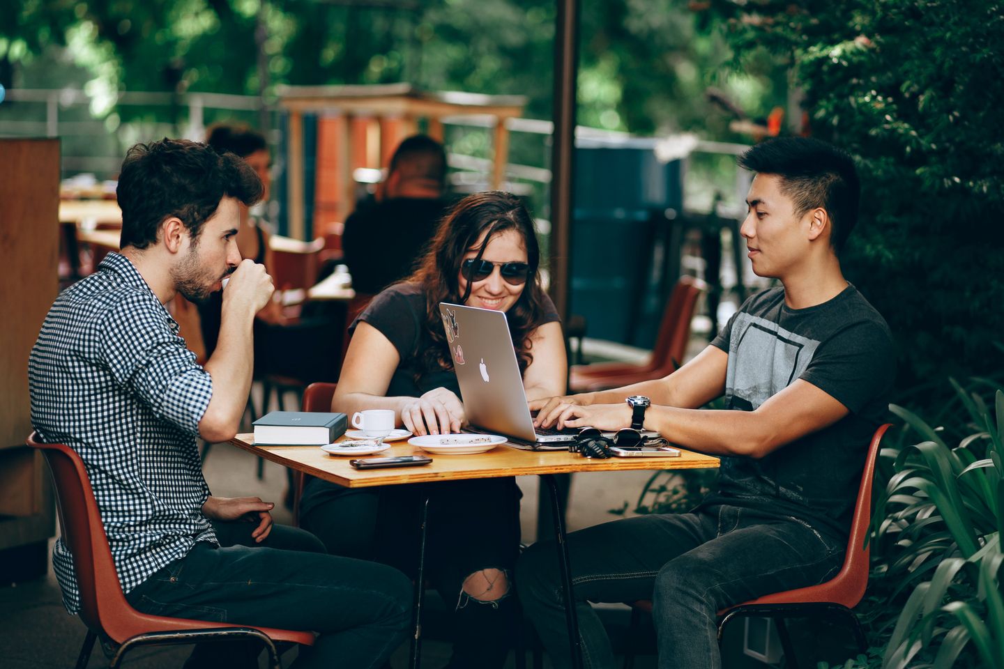 A group of three friends chatting and studying around a table on the patio of a coffee shop