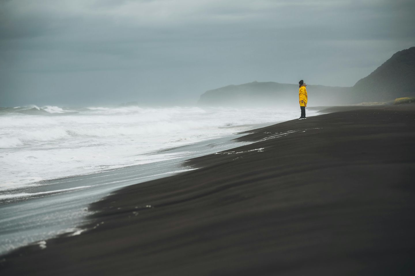 a person in a raincoat views heavy surf at a black sand beach