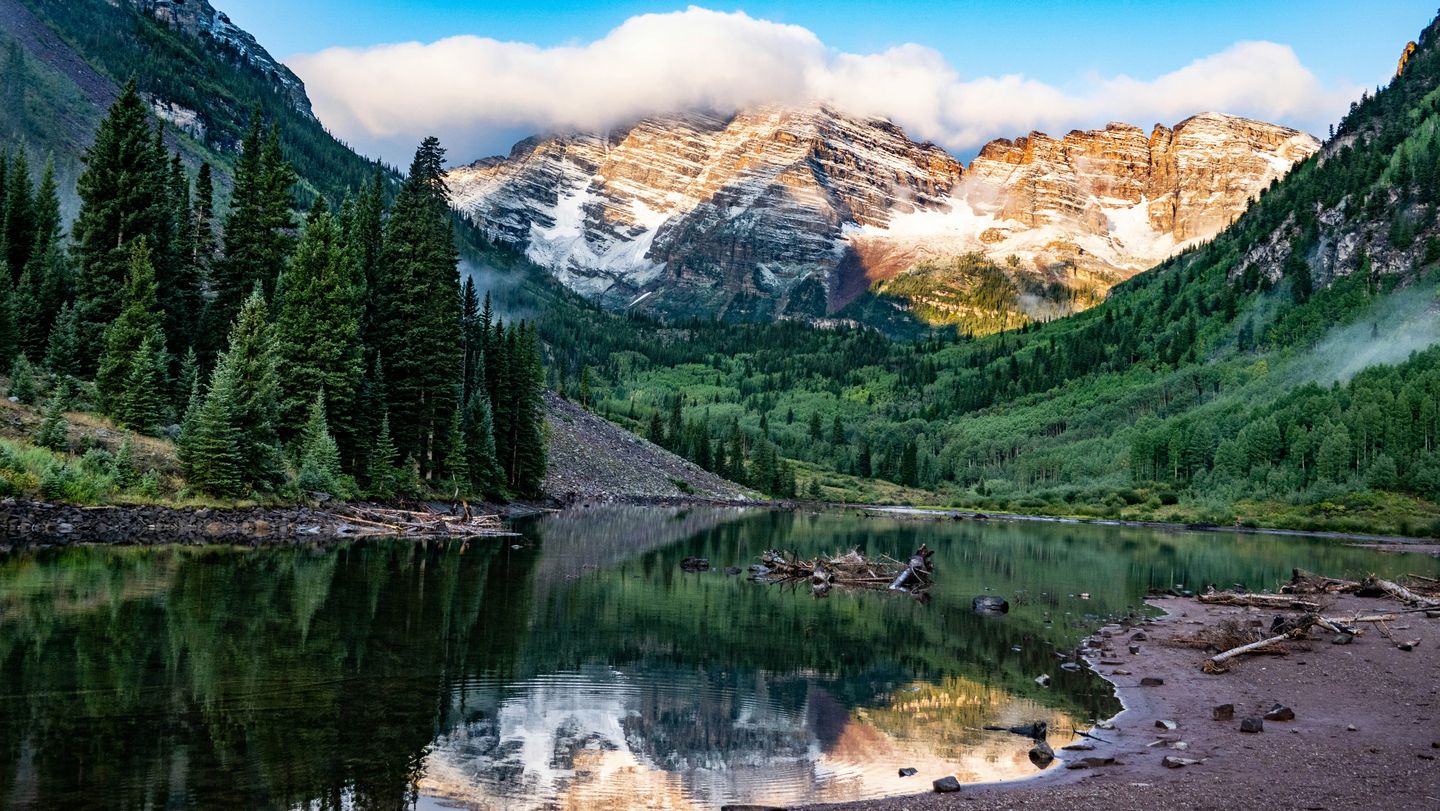 A valley lake in between mountains with conifers along the shore in Maroon Bells, Colorado, USA