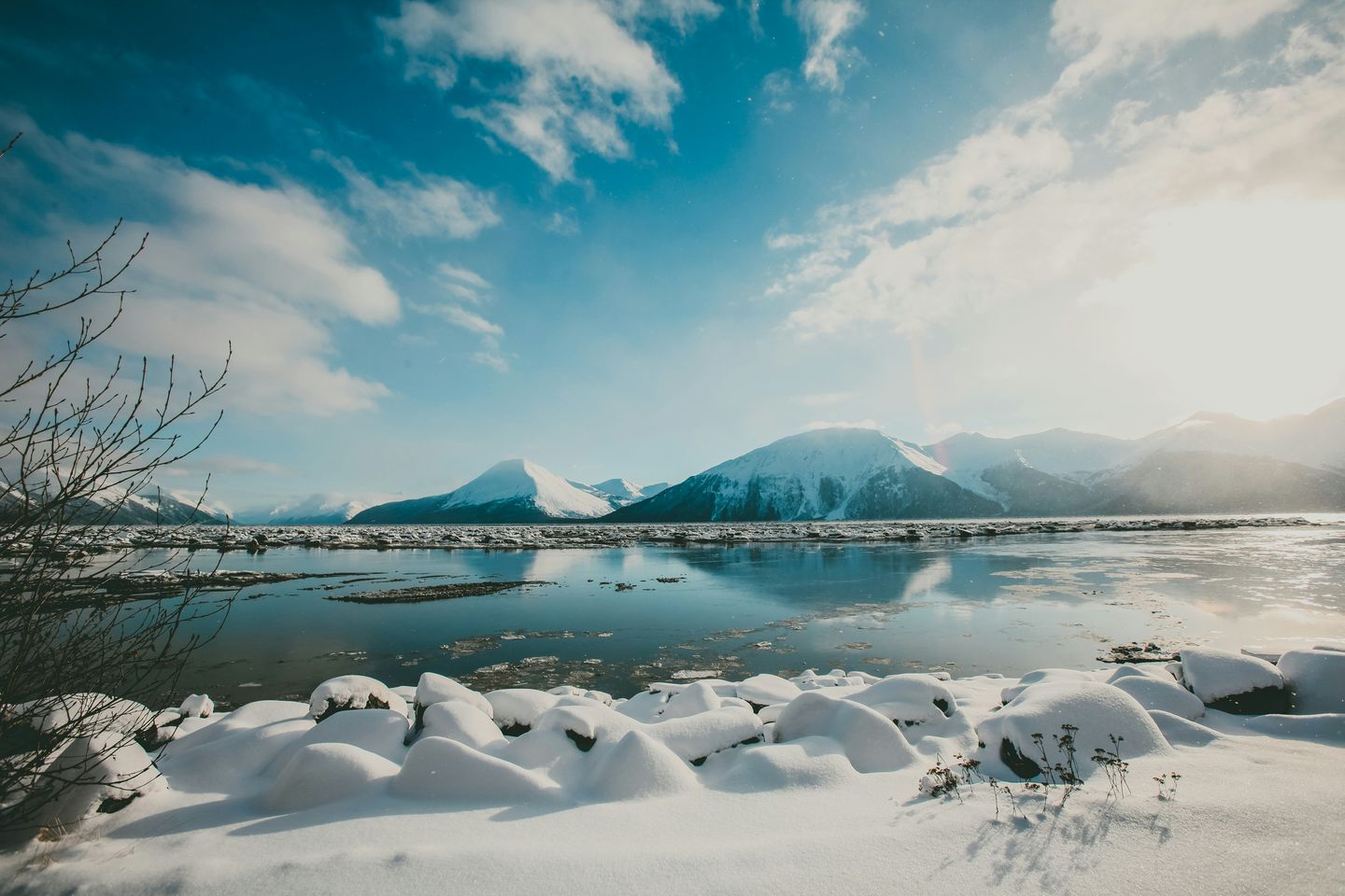 Snowcapped mountains under a clear blue sky in front of a large body of water in Alaska, USA