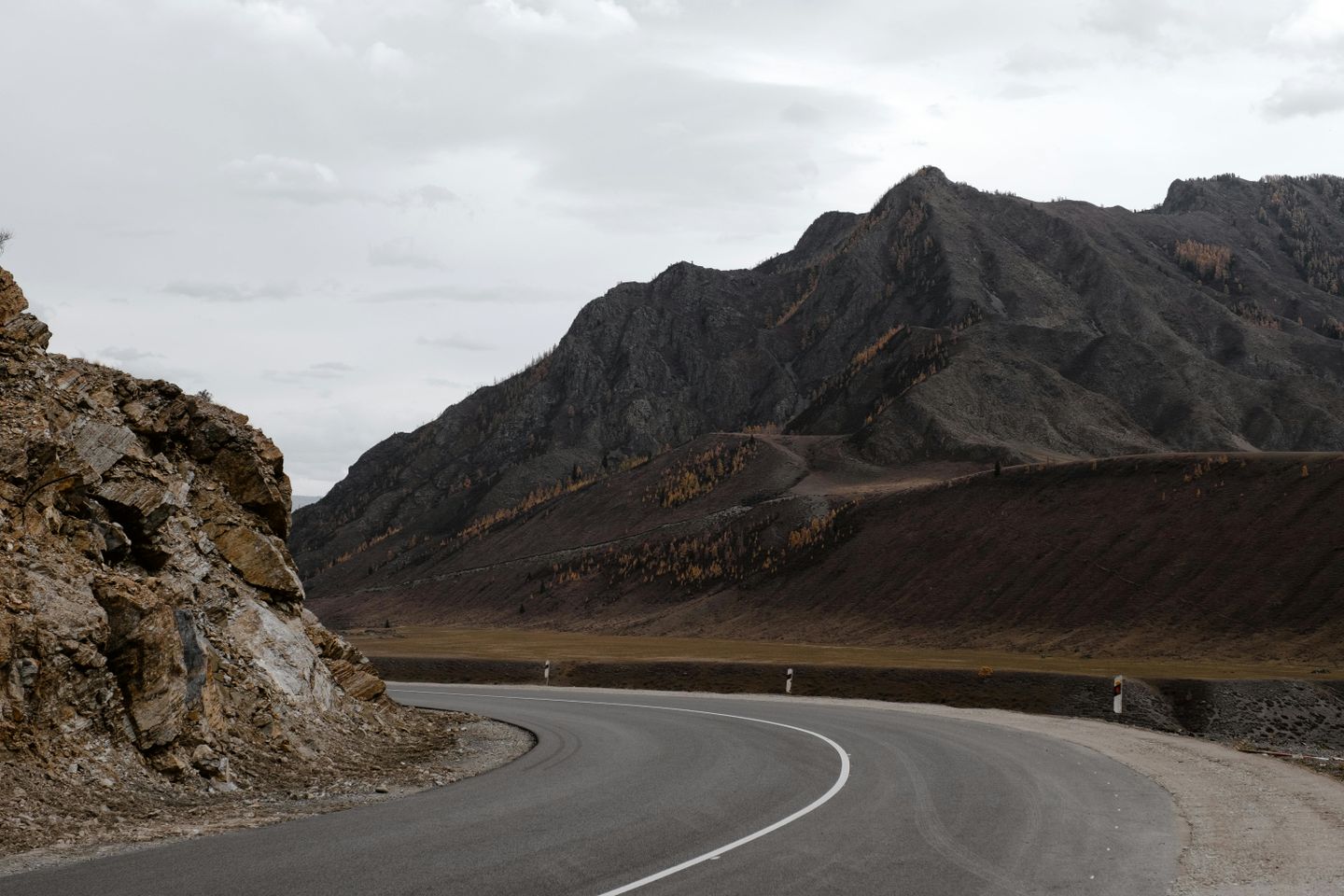 a highway cutting through rugged black mountains in Russia