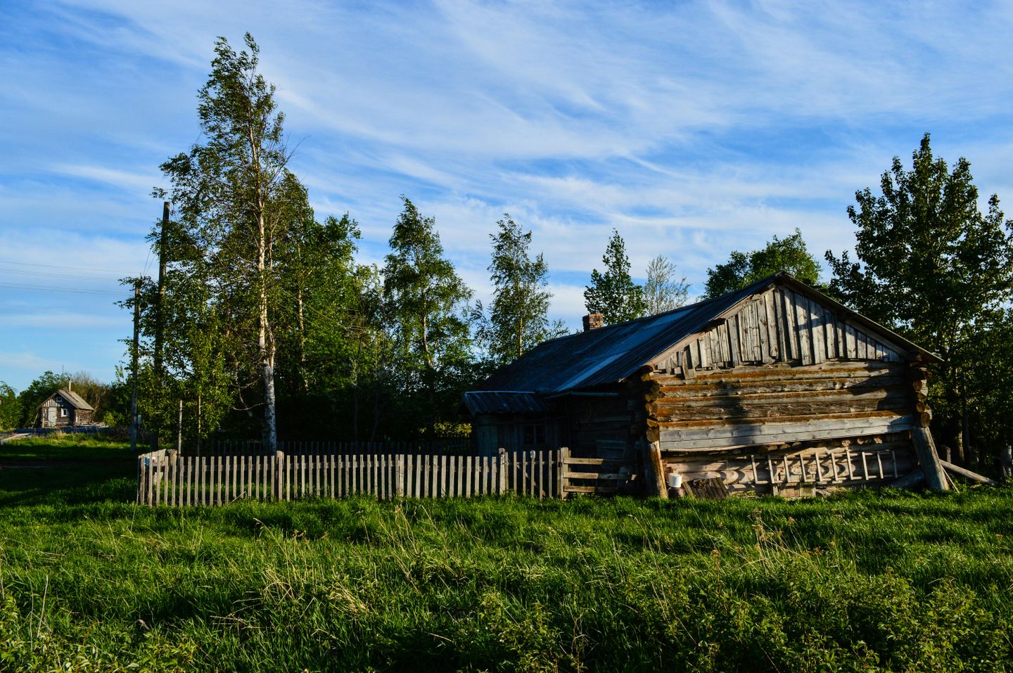 An old, unpainted wooden barn at the edge of a field on a sunny day.