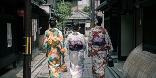 Three women in traditional silk garb walking down a historic Japanese street
