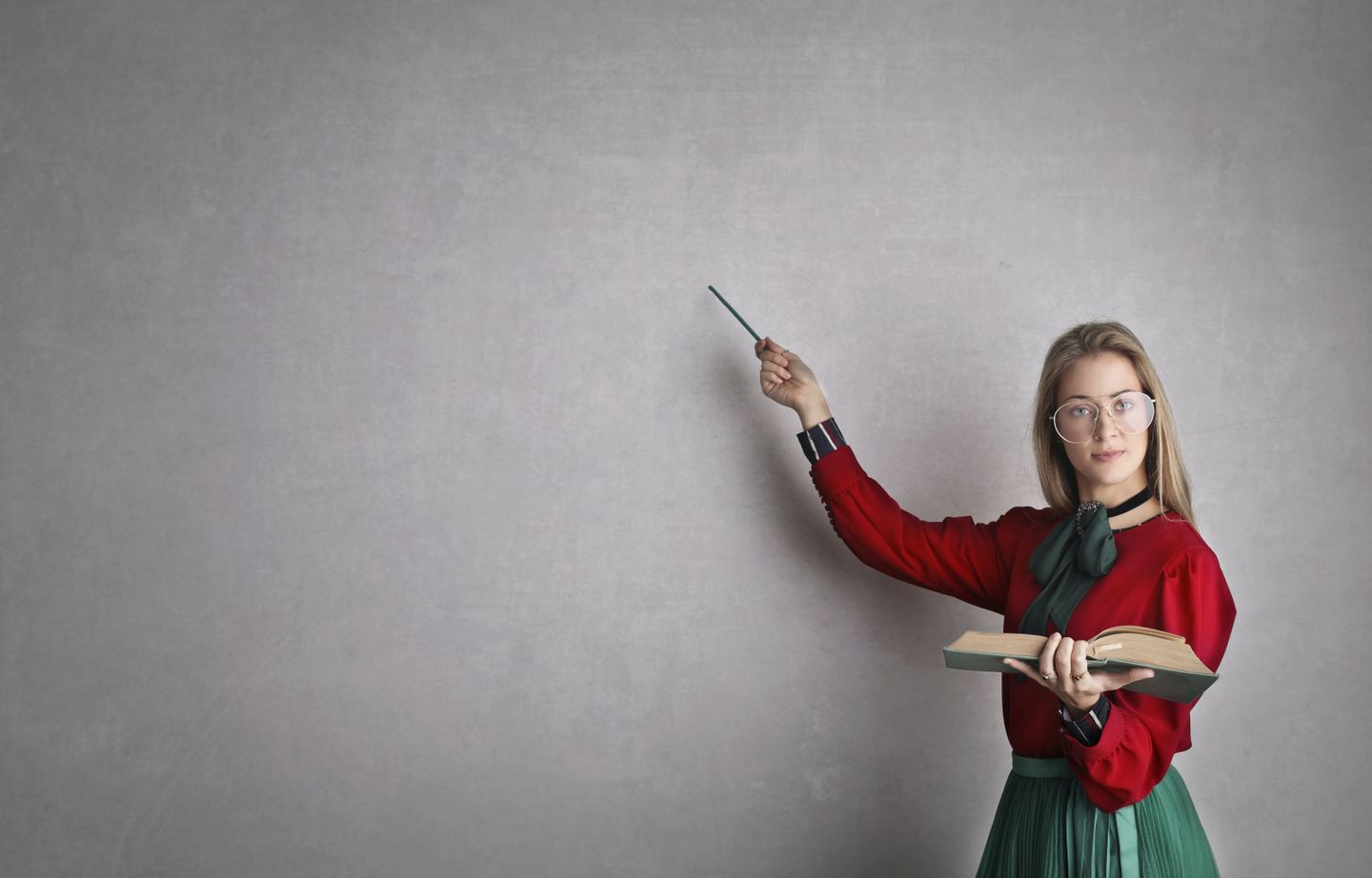 A woman holding a book points to a chalkboard