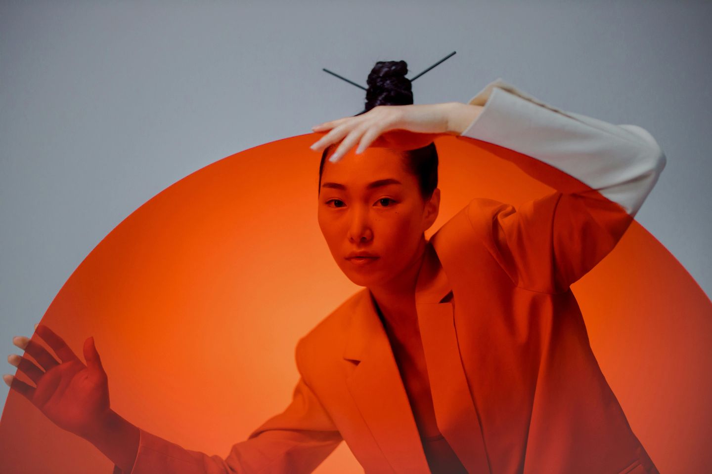 a female Japanese model posing in a white suit behind a huge circle of red glass reminiscent of the Japanese flag