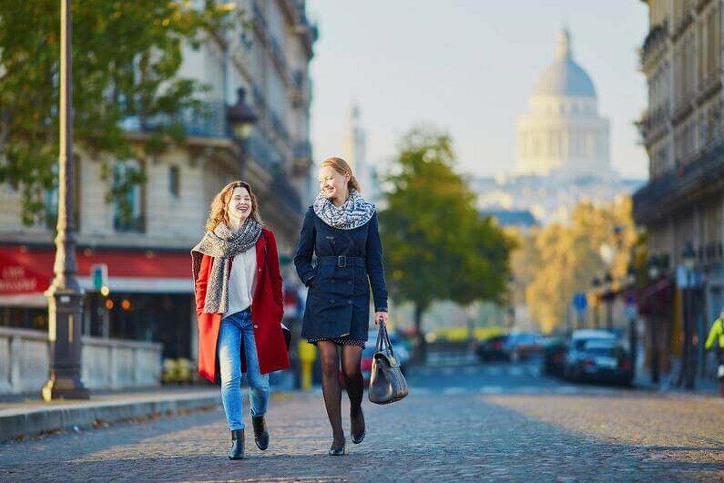 Two women dressed in nice clothes walking down the street, talking and smiling