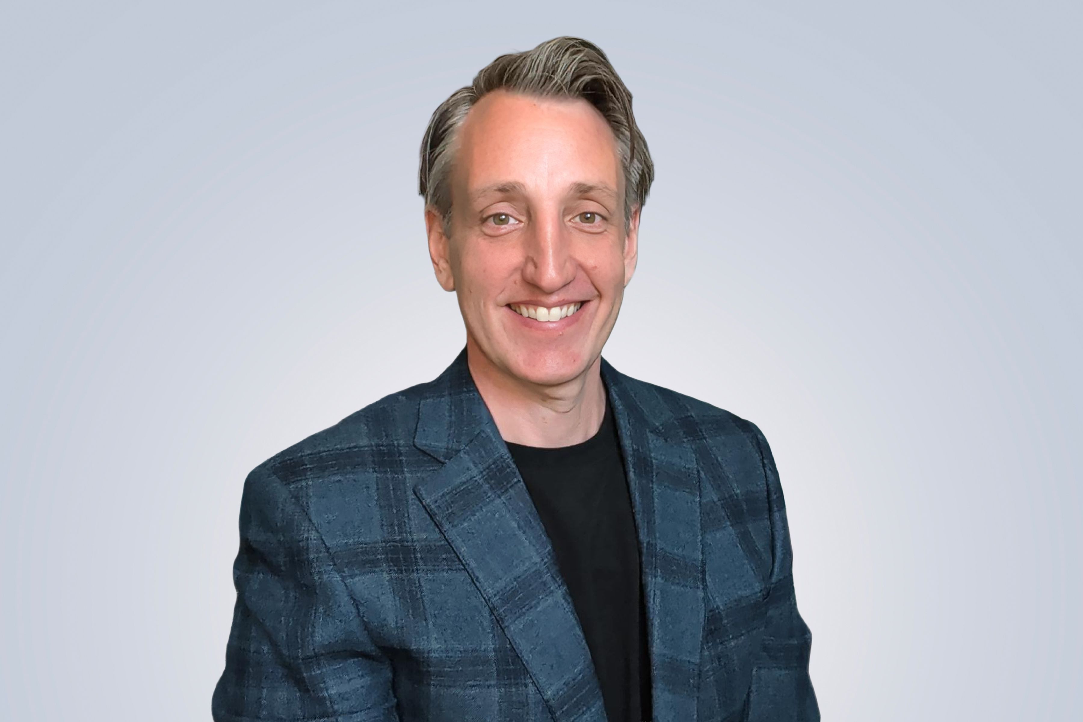 Smiling man in a blue plaid blazer and black shirt against a light gradient background.