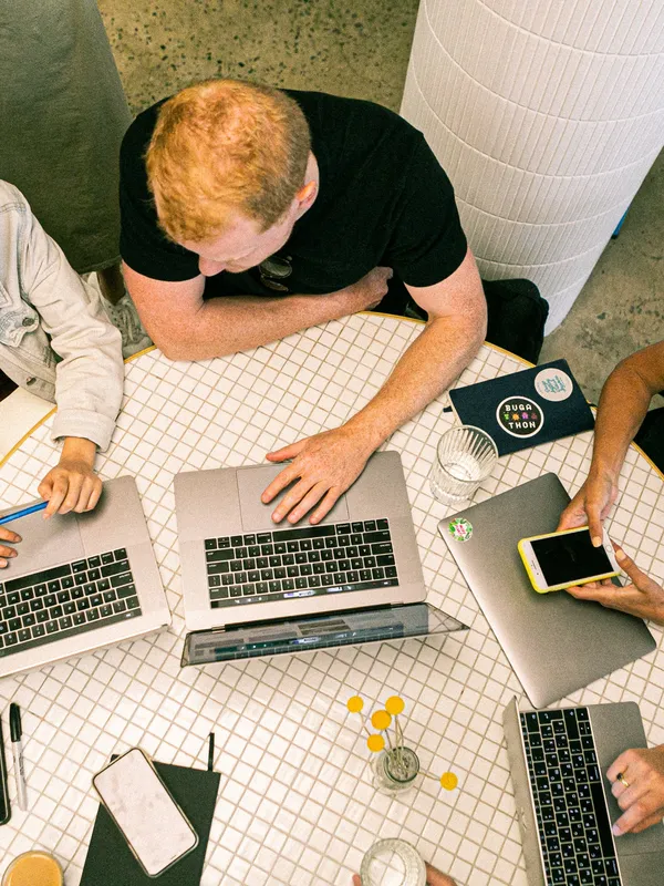 group of people sitting at a table with laptops, books and papers