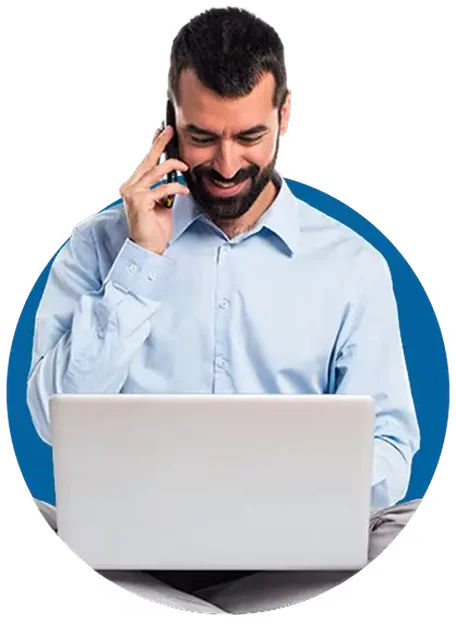 Man in a light blue shirt talking on a phone and smiling while using a laptop. Blue circular background.