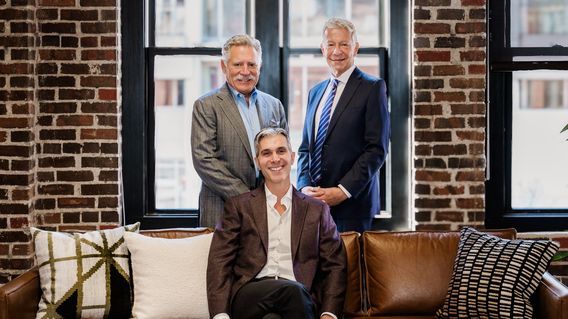 three men in suits grouped together smiling at camera