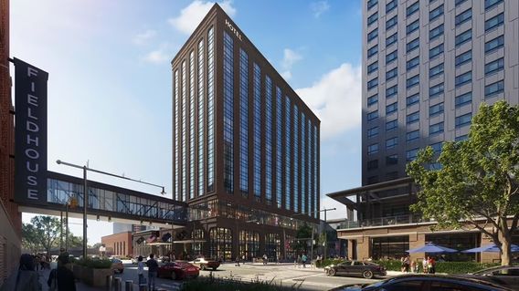 Street view of a modern cityscape with tall glass buildings, a skywalk, and pedestrians. Cars are on the road, and a tree is in the foreground.