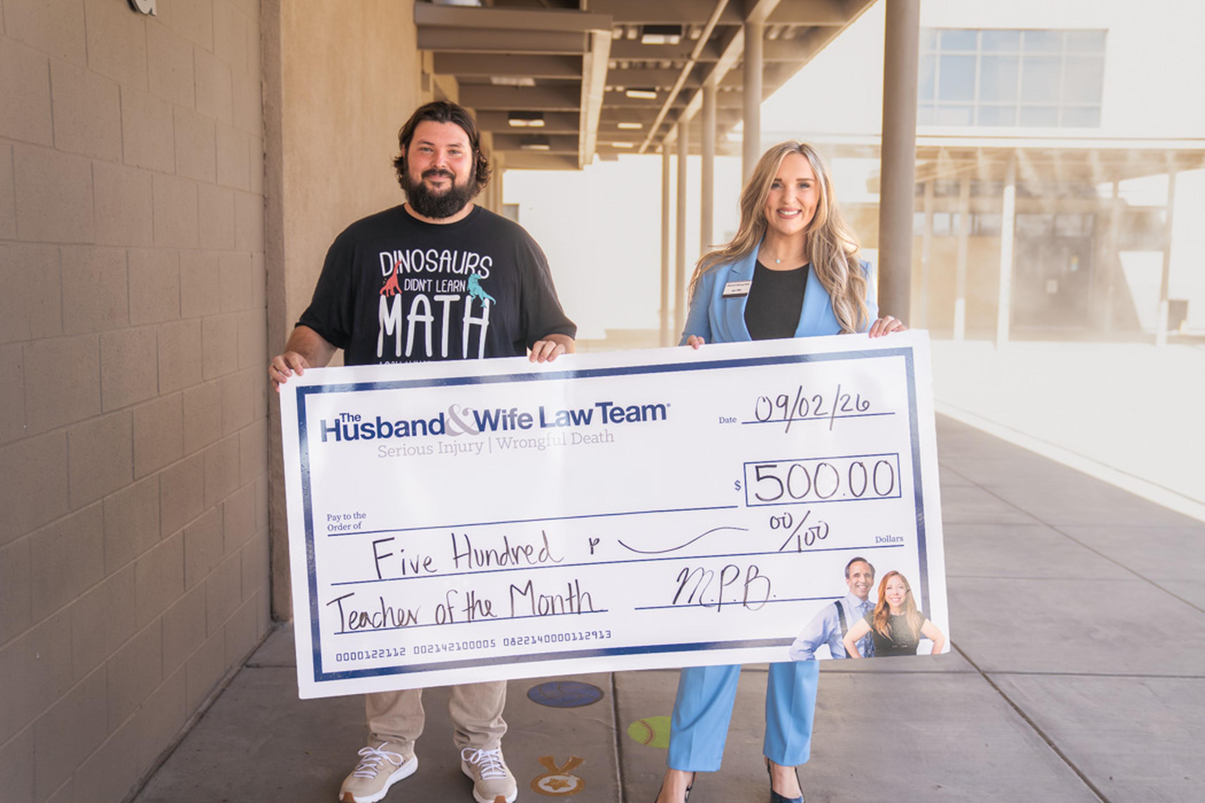 Jen from the Husband & Wife Law Team presents Mr. Knowles with a $500 Teacher of the Month award, recognizing his dedication and positive impact on students at Val Vista Academy.