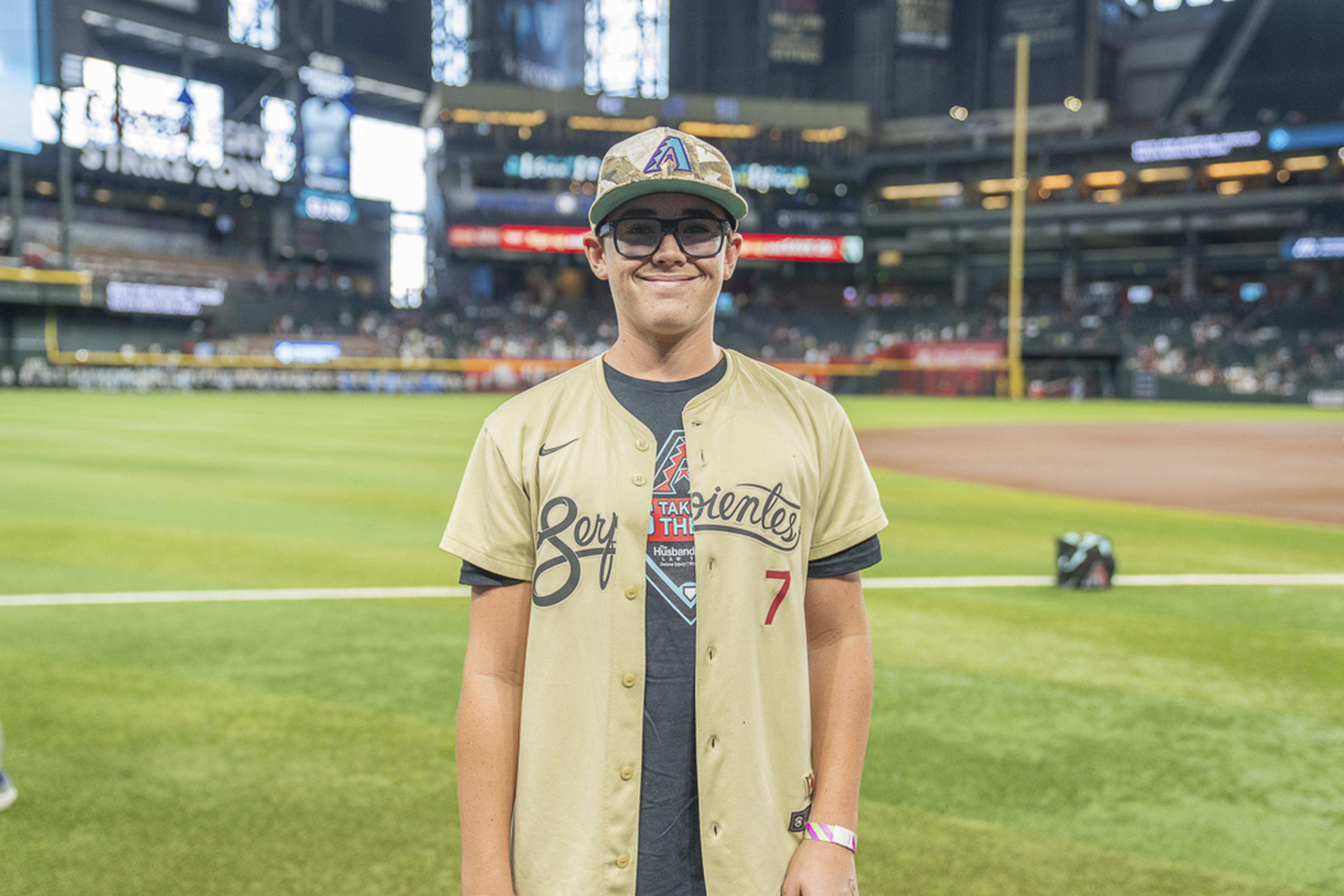 Wearing a baseball jersey and cap, a young fan enjoys his moment on the field during the Kids Take the Field experience, creating memories that will last a lifetime.