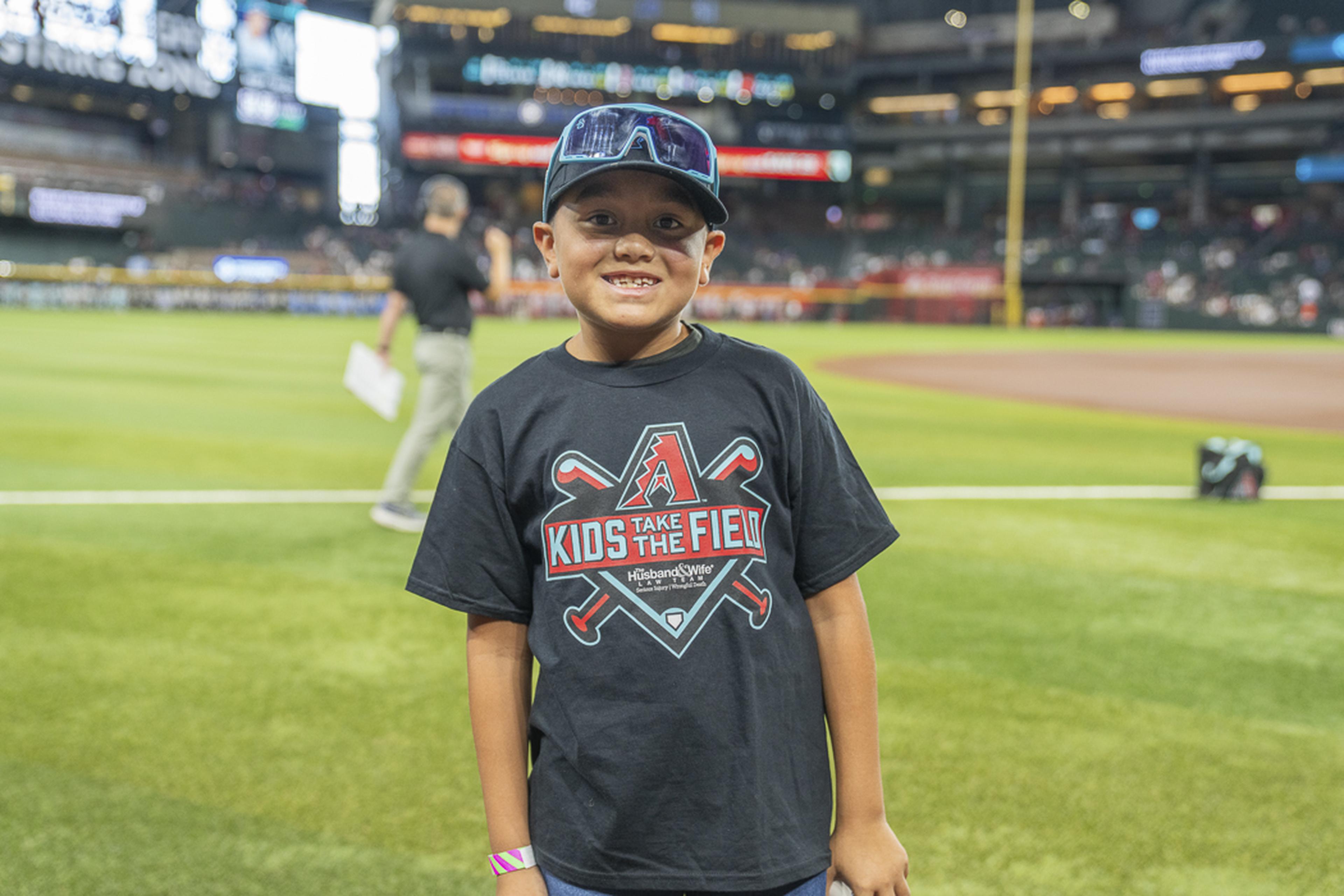A young Kids Take the Field participant smiles proudly on the field, taking in the excitement of a once-in-a-lifetime experience at Chase Field beneath the bright stadium lights.