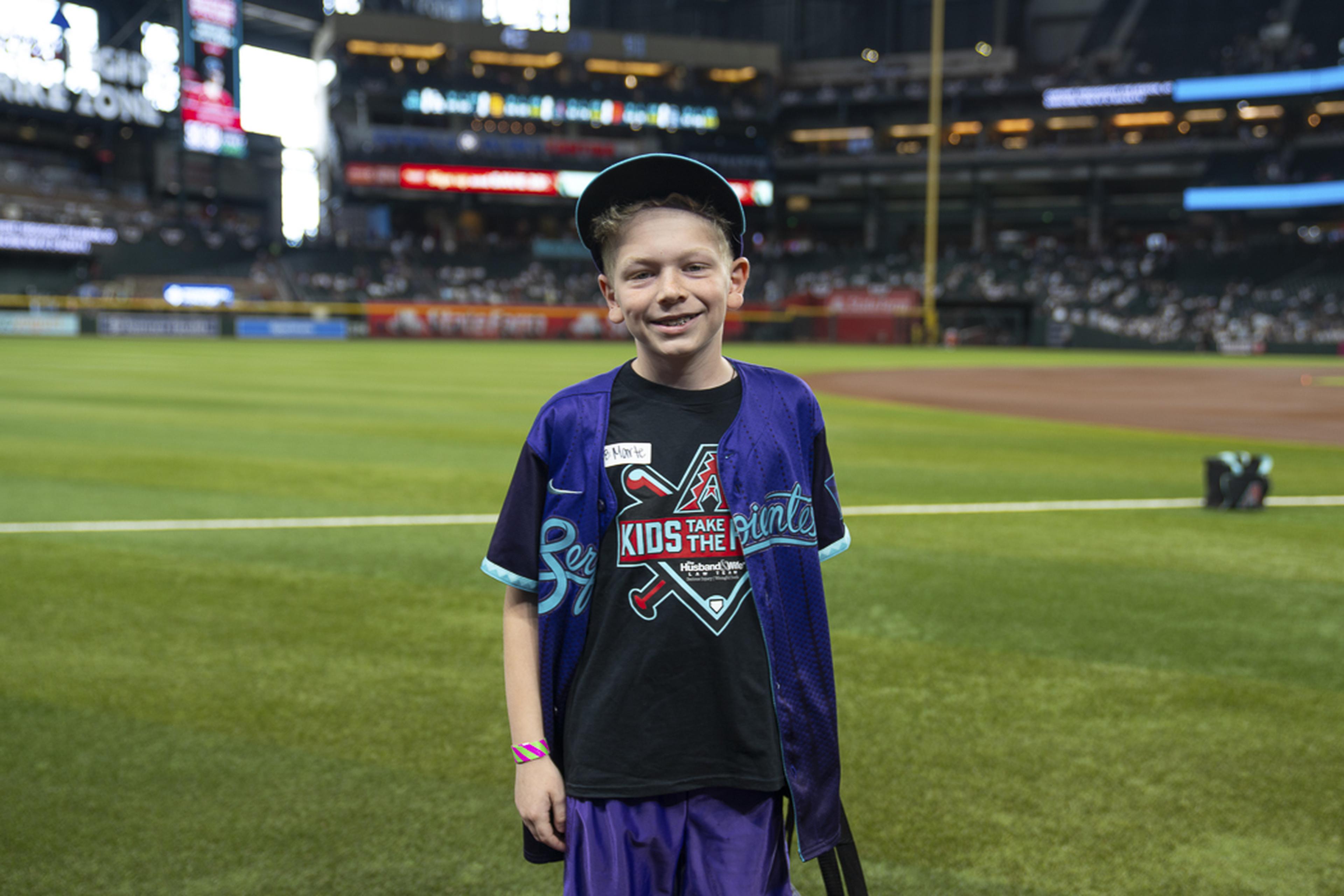 A young fan smiles on the field at Chase Field, enjoying a memorable Kids Take the Field experience with the excitement of game day all around him.