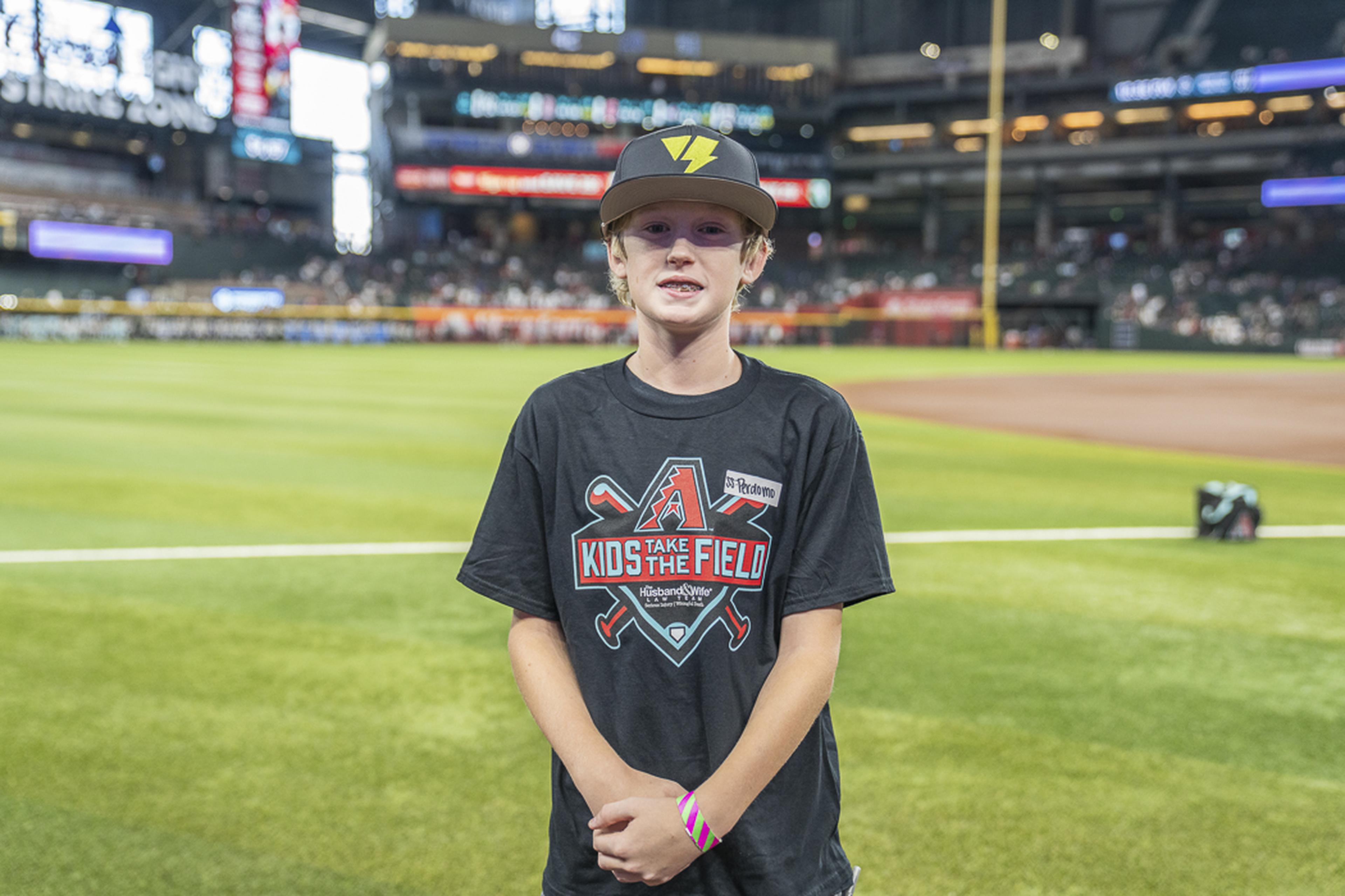 A young Kids Take the Field participant stands proudly on the field, taking in the excitement of a game-day experience at Chase Field with the stadium crowd in the background.