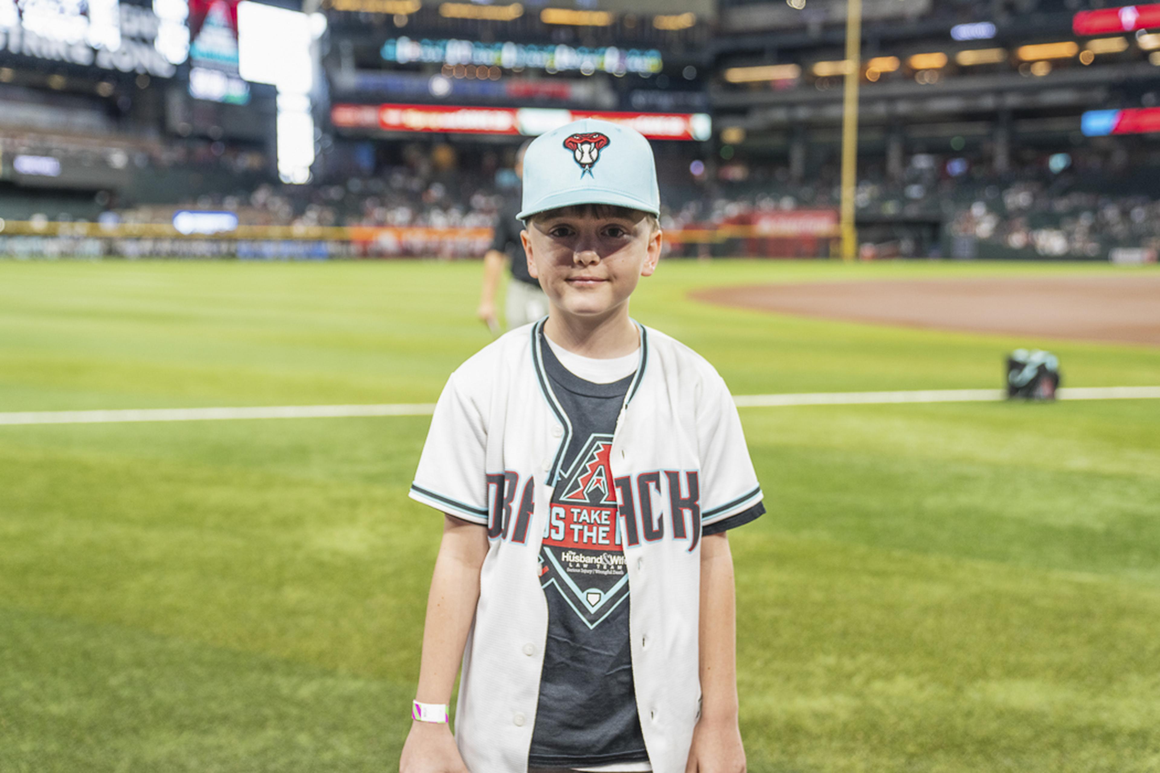 Wearing his baseball jersey and cap, a young fan enjoys a memorable moment on the field, creating lasting memories during the Kids Take the Field experience.