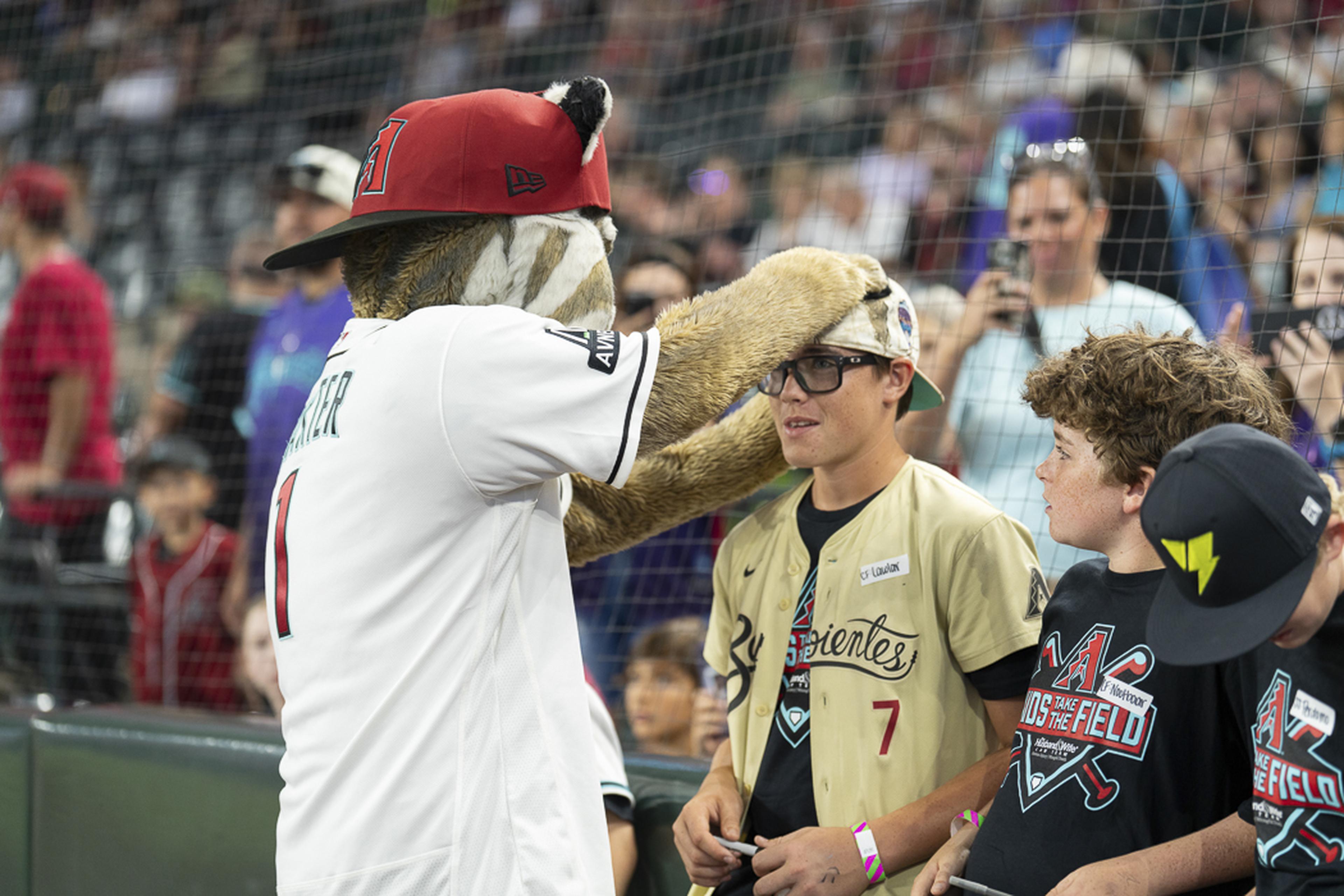Baxter, the Arizona Diamondbacks mascot, shares a playful moment with a young fan, adjusting his cap and adding to the excitement of an unforgettable Kids Take the Field experience.