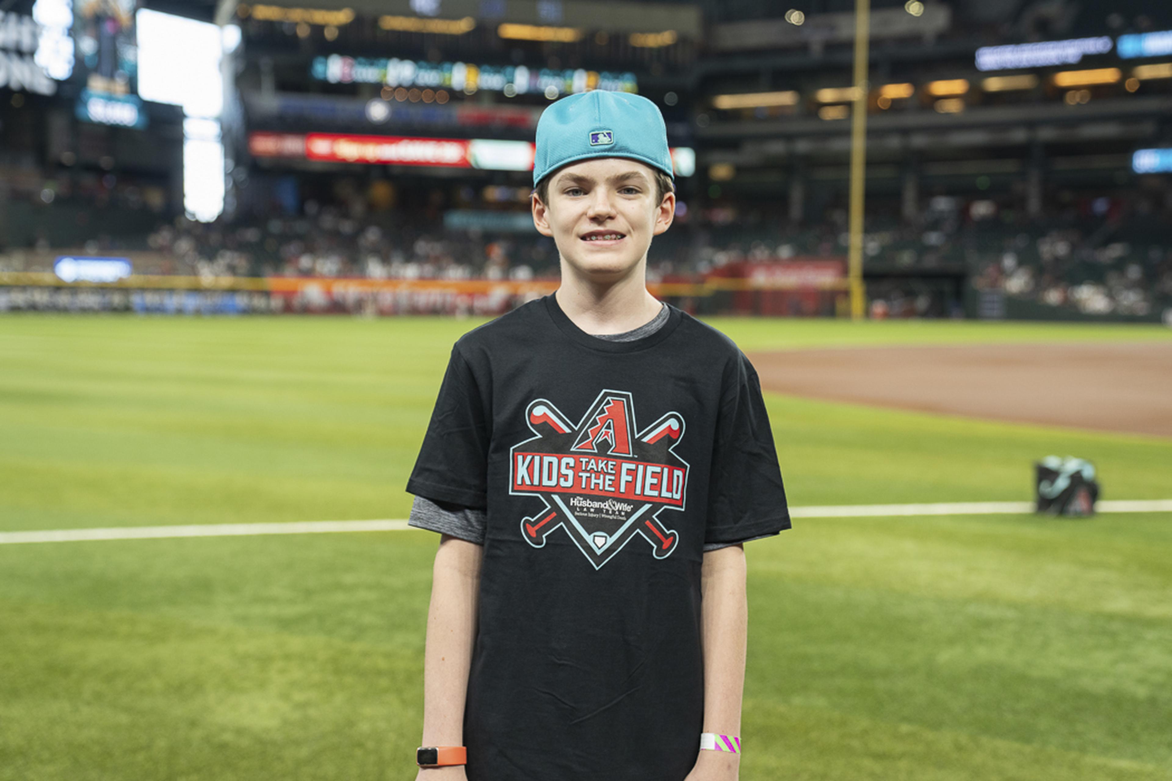 A young Kids Take the Field participant smiles on Chase Field, enjoying a once-in-a-lifetime opportunity to stand where the pros play.