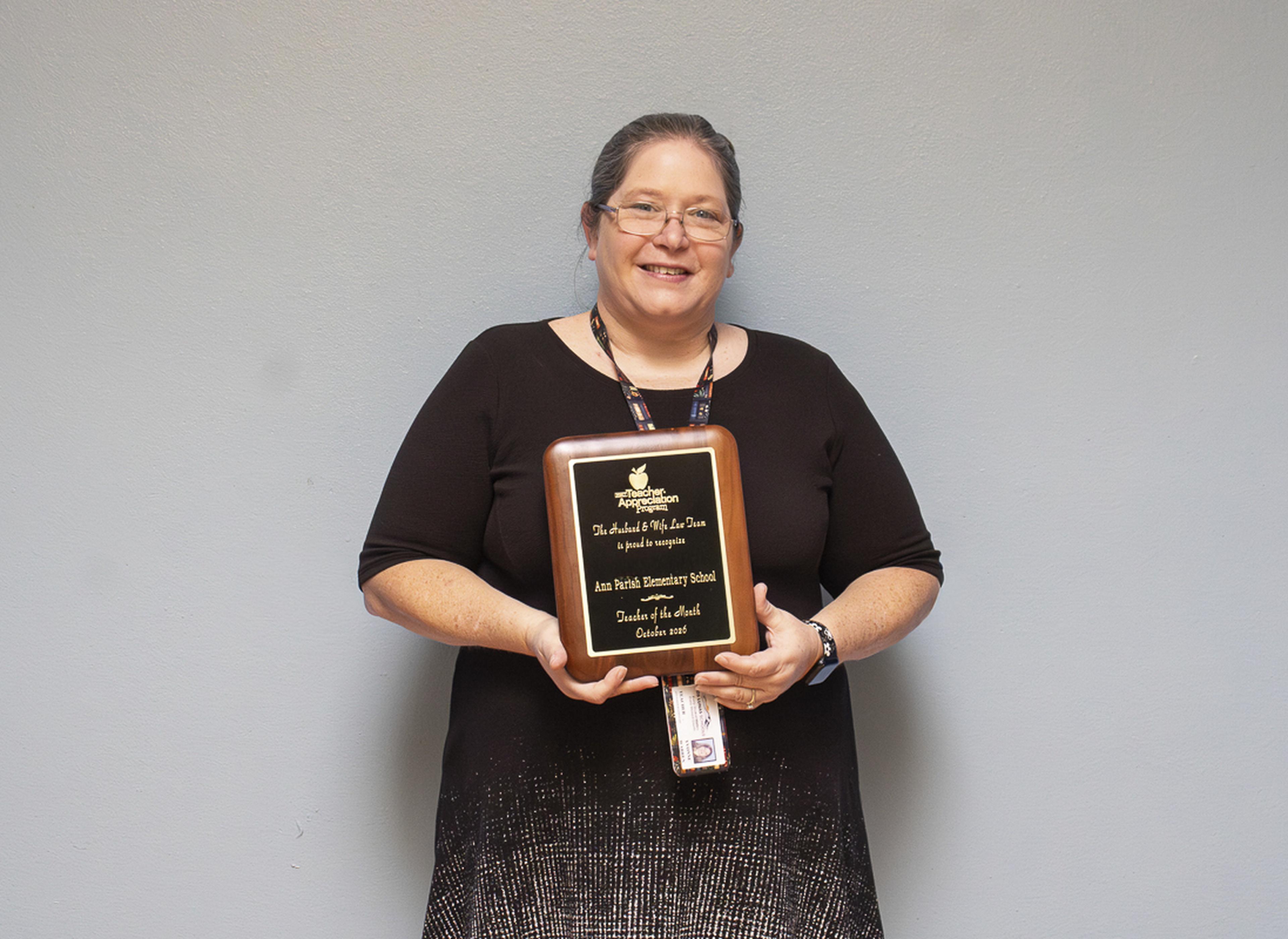 Mrs. Warren beams with excitement as she waves and proudly shows off her Teacher of the Month award at Ann Parish Elementary School.