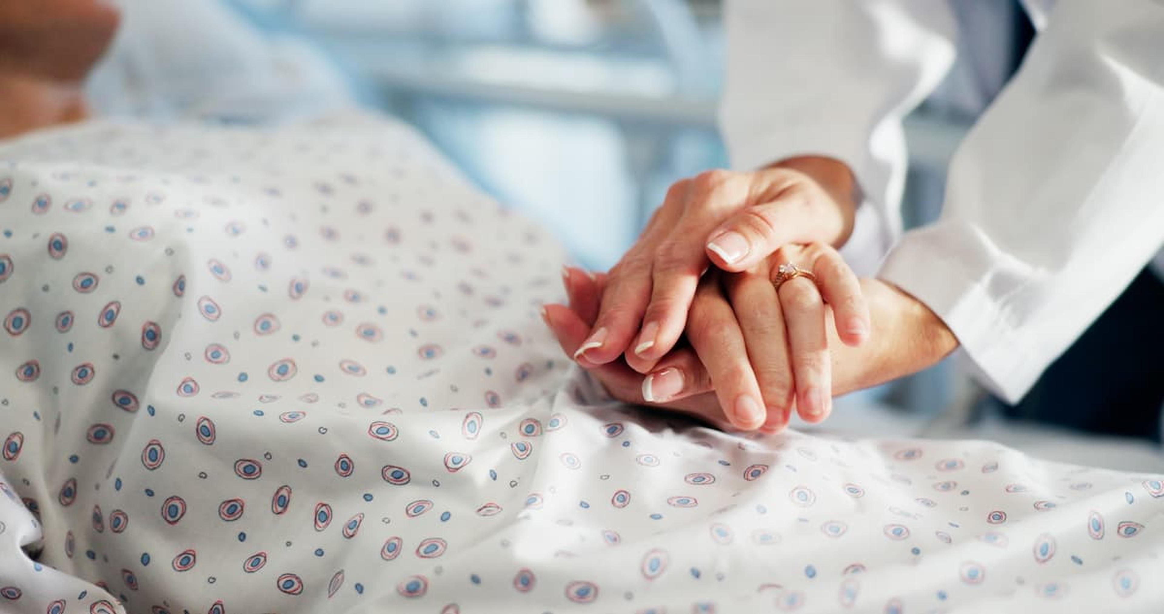 A doctor comforting a patient by holding their hand, showing empathy and care. The patient is covered with a patterned hospital gown.