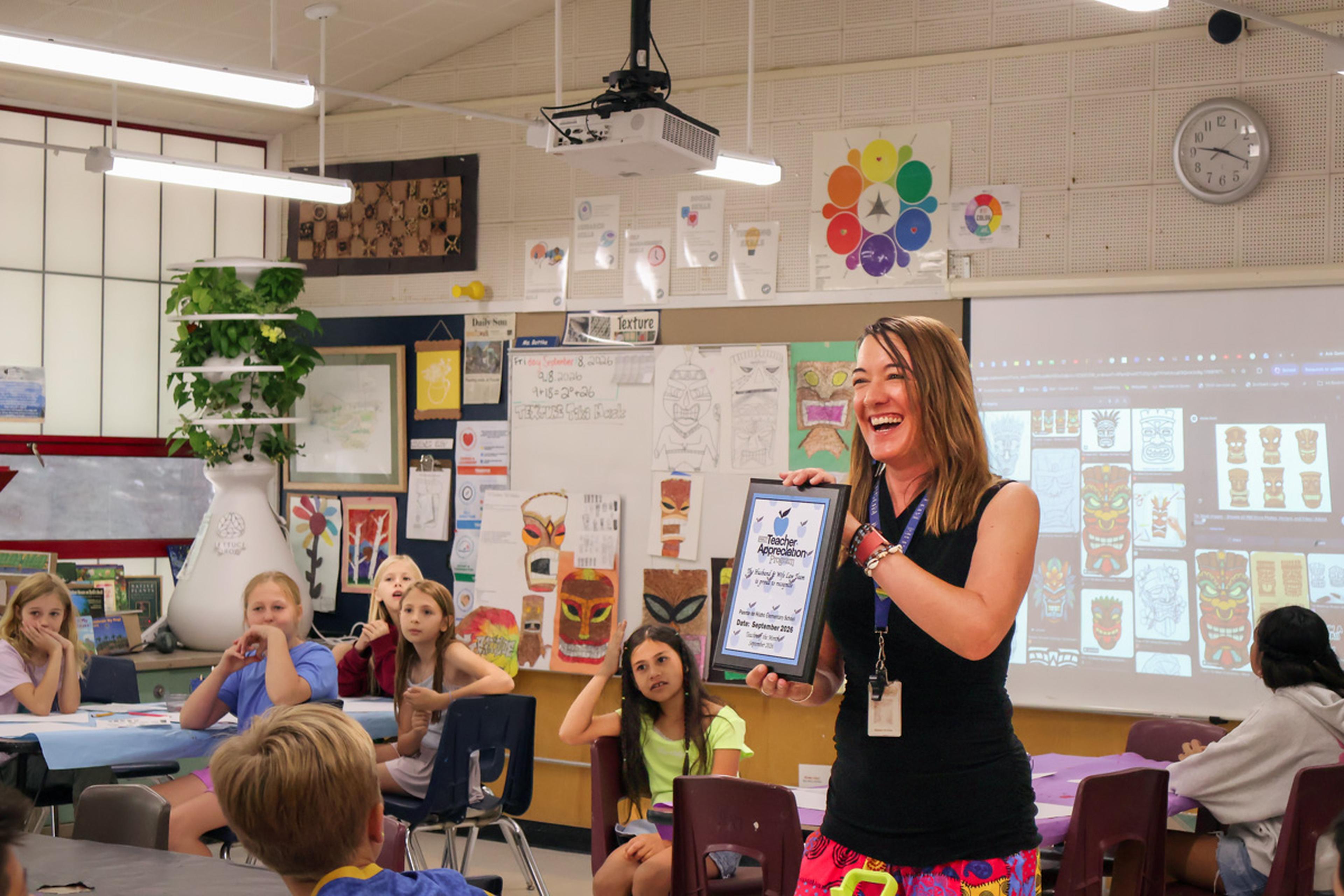 Ms. Bottke proudly displays her Teacher Appreciation Award from the Husband & Wife Law Team while surrounded by her students, recognizing her dedication to creating a positive and engaging learning environment at Puente de Hózhó Elementary.