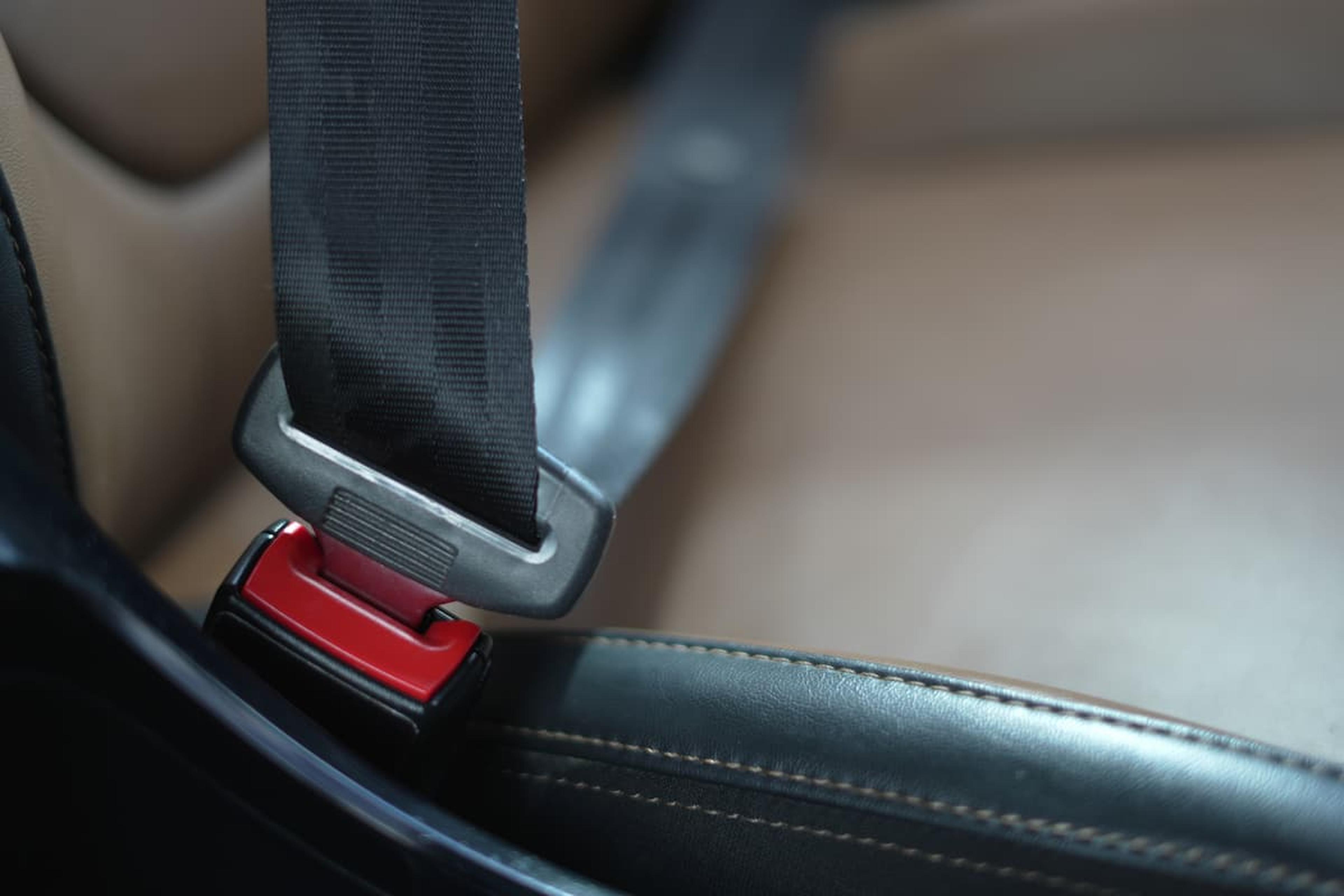 A close-up of a fastened black seatbelt in a car seat, with visible red buckle and brown upholstery.