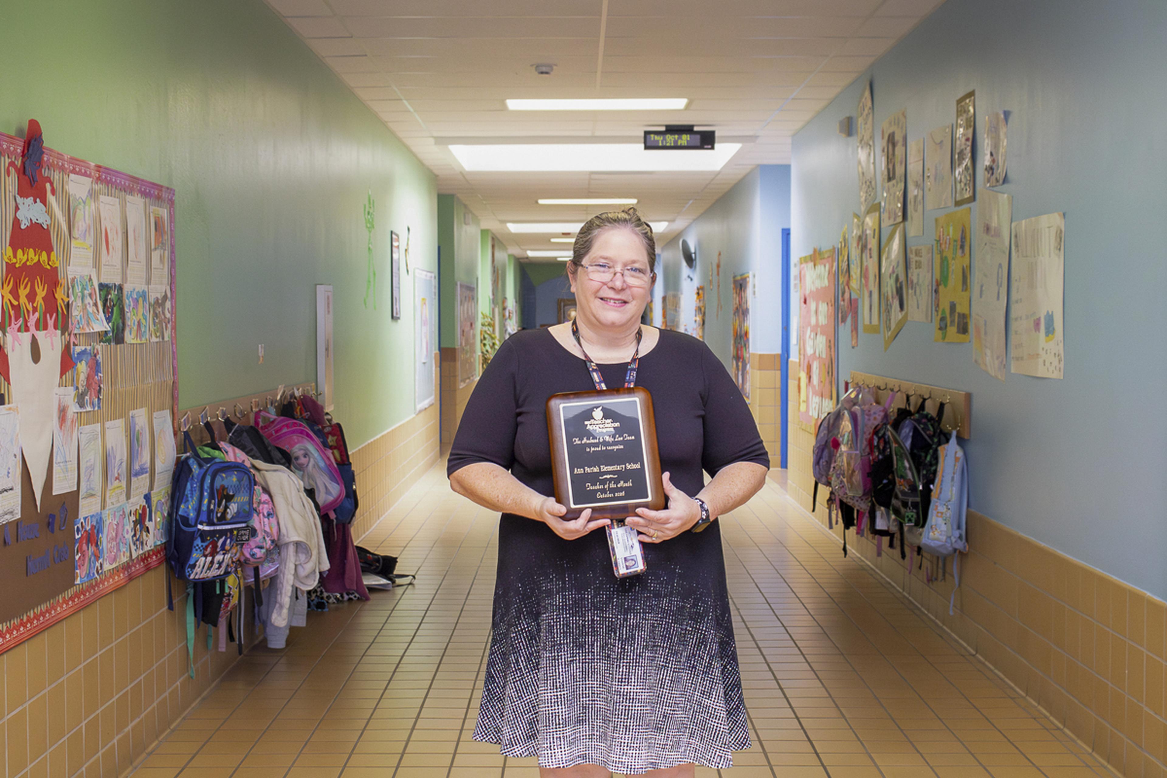 Mrs. Warren proudly displays her Teacher of the Month plaque in the colorful halls of Ann Parish Elementary School, celebrating a well-deserved honor.