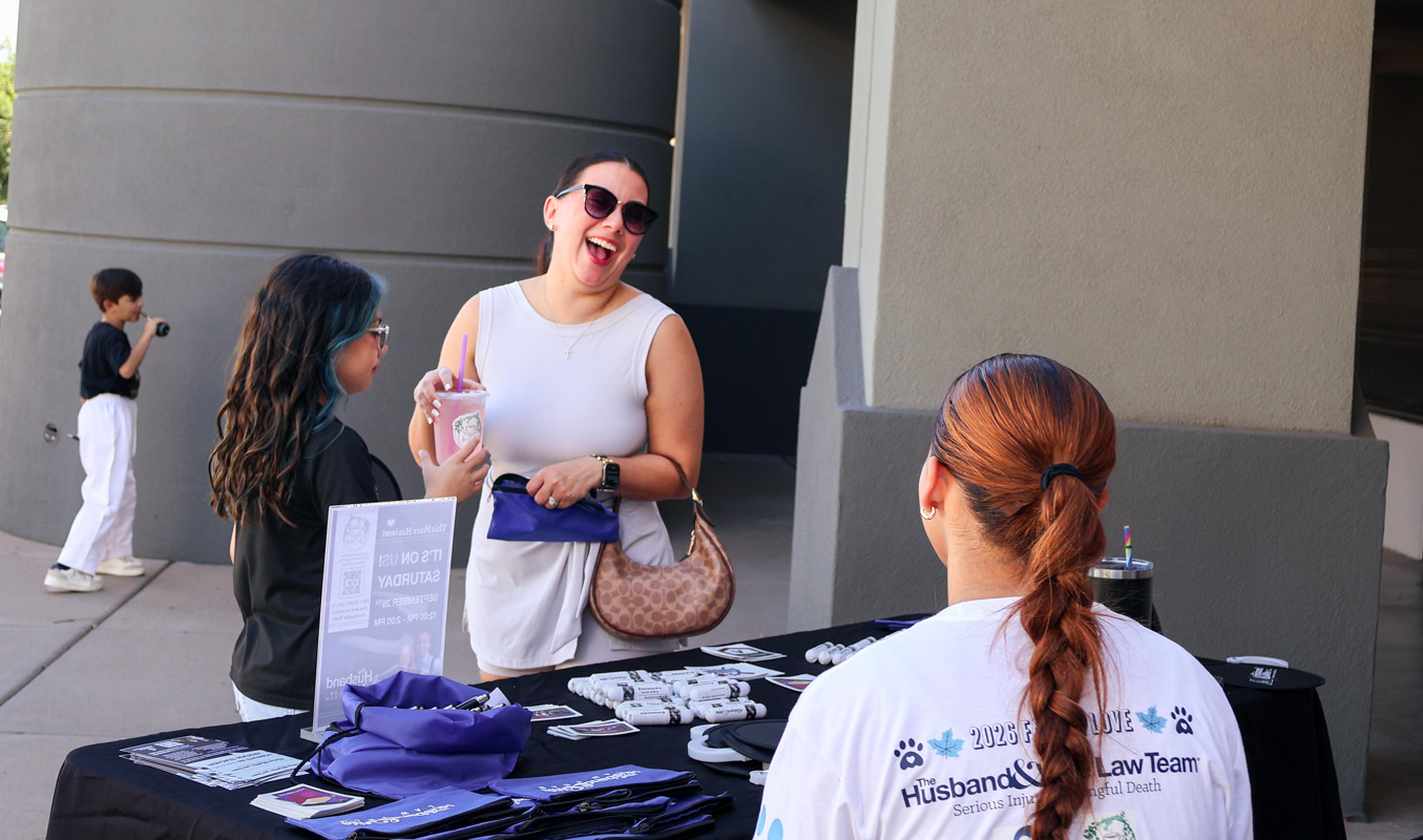 Two attendees share smiles and conversation at the Husband & Wife Law Team’s HALO Adoption Event, welcoming community members and supporting the mission of helping pets find loving homes.